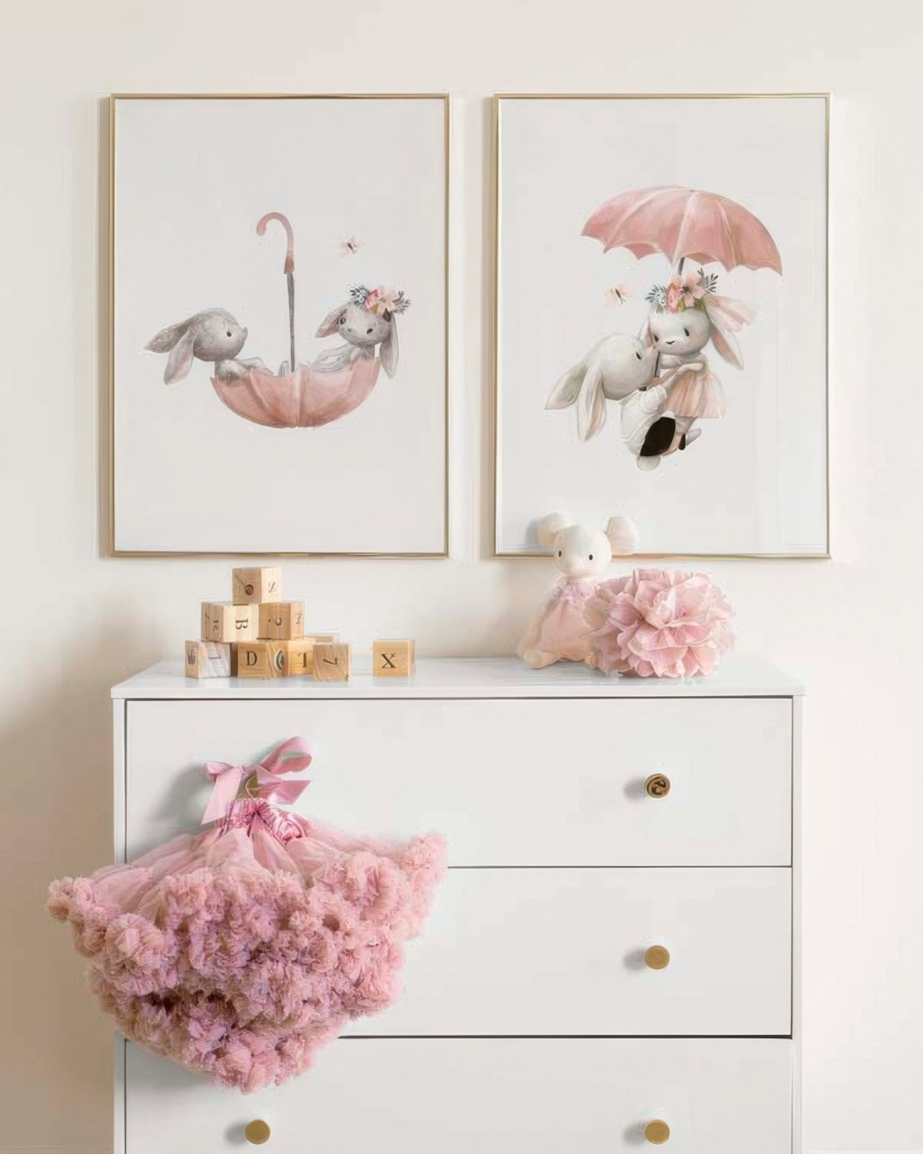 Ett posterpaket med två kaniner i rosa lekfulla motiv, upphängda ovanför en vit byrå i ett barnrum.