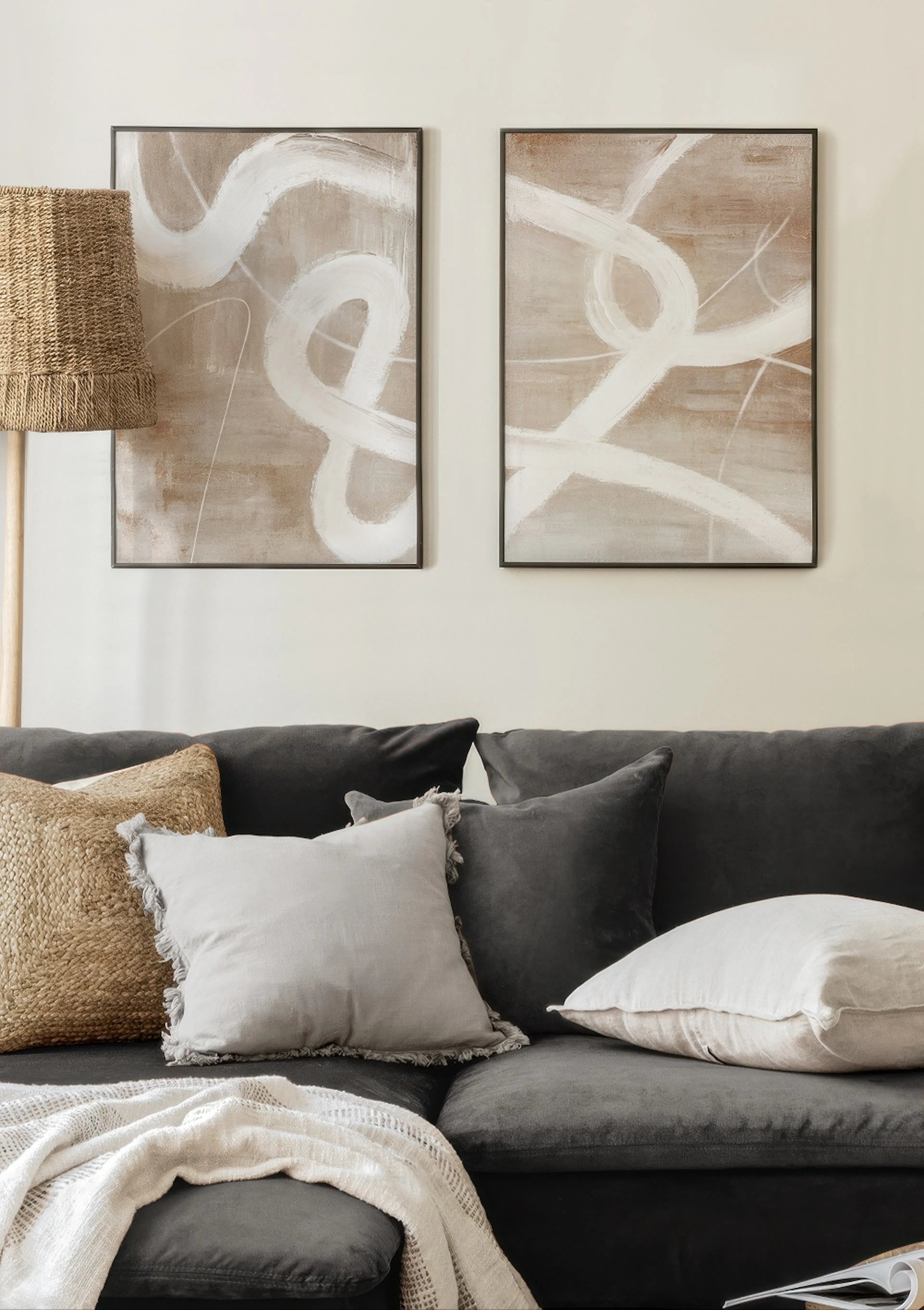 Twee postersets met abstracte witte penseelstreken op een beige achtergrond, hangend boven een donkere bank.