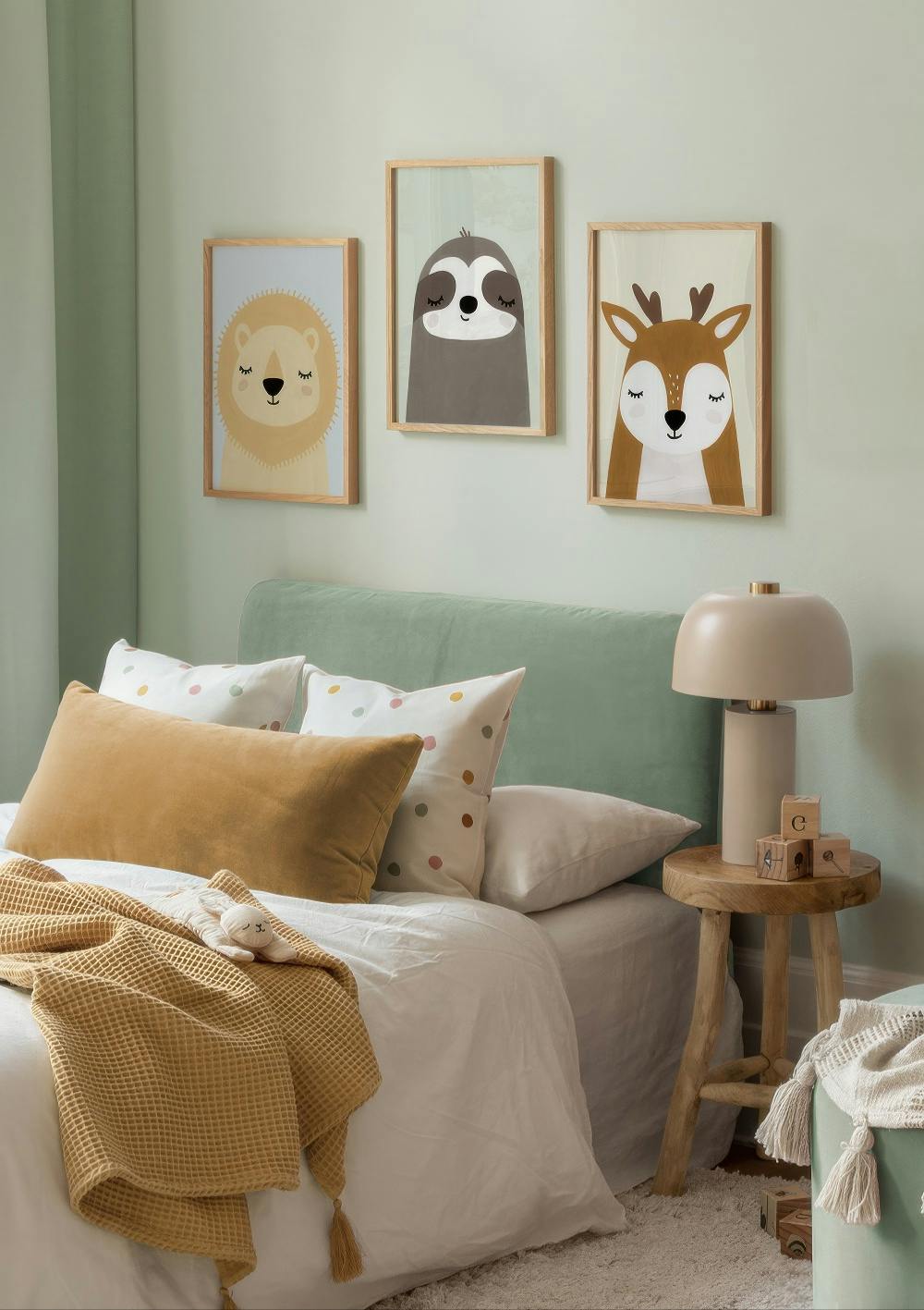 A poster pack featuring three framed animal prints: a lion, a sloth, and a deer, above a bed in a childs room.