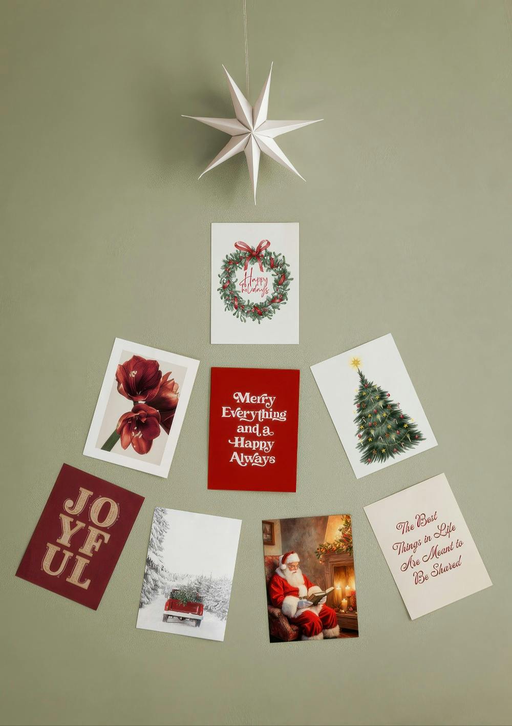 A Christmas poster pack featuring festive designs like a wreath, Santa, and a Christmas tree, arranged on a sage green wall.