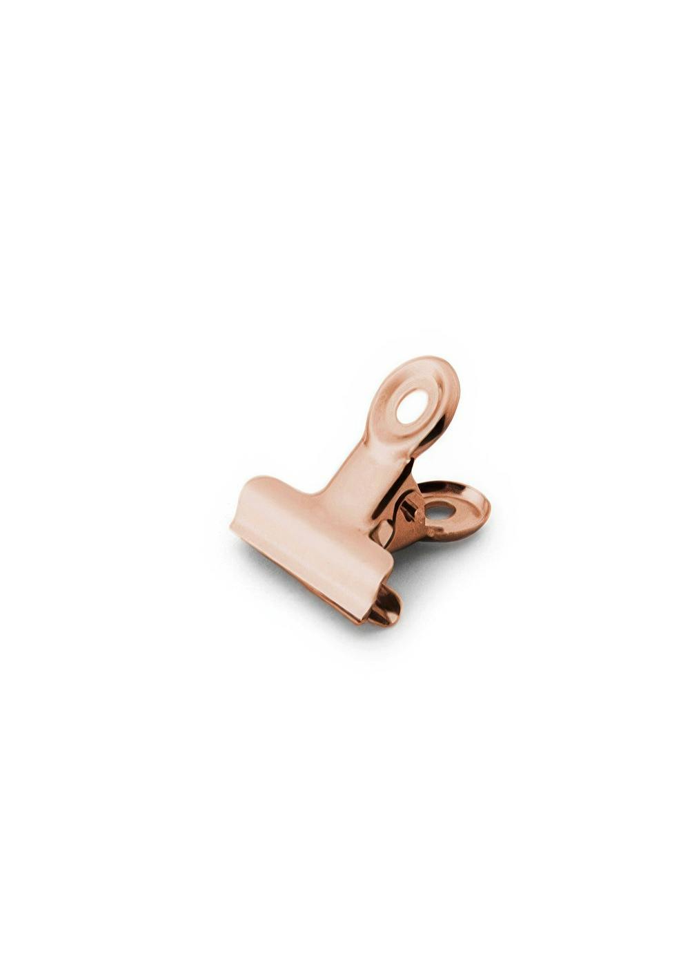 Een poster van een glimmende, roségouden binderclip, liggend op een witte achtergrond.