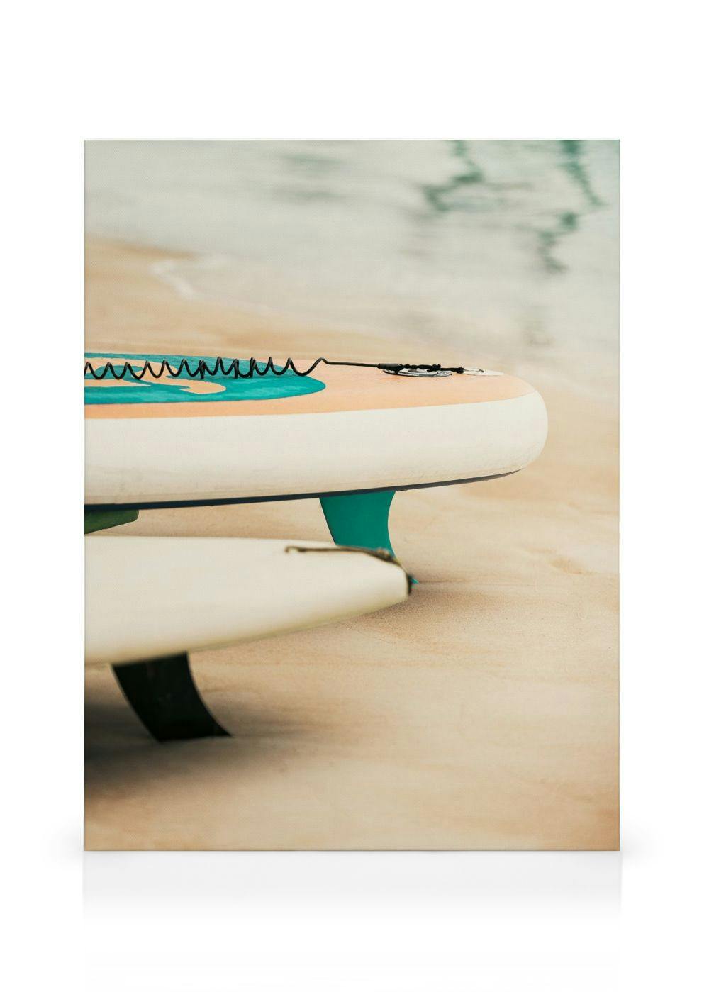 Leinwandbild von zwei Surfbrettern mit Finnen im Sand am Meer, eine schwarze Leine liegt auf dem oberen Board.