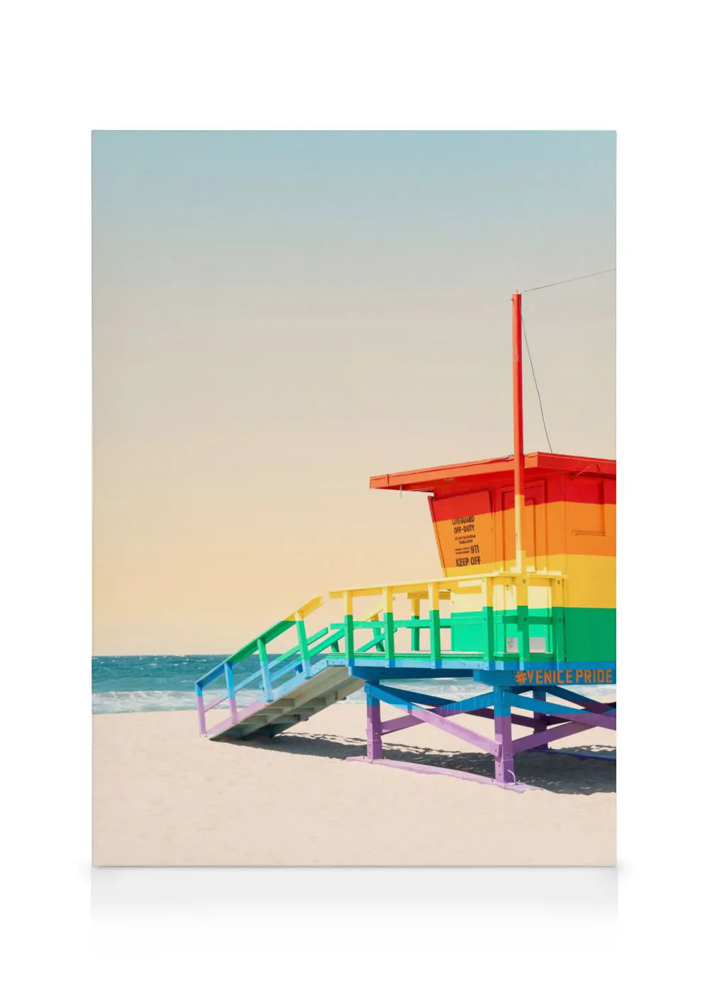 A canvas showing a rainbow-coloured lifeguard hut on a sandy beach by the ocean under a clear sky.