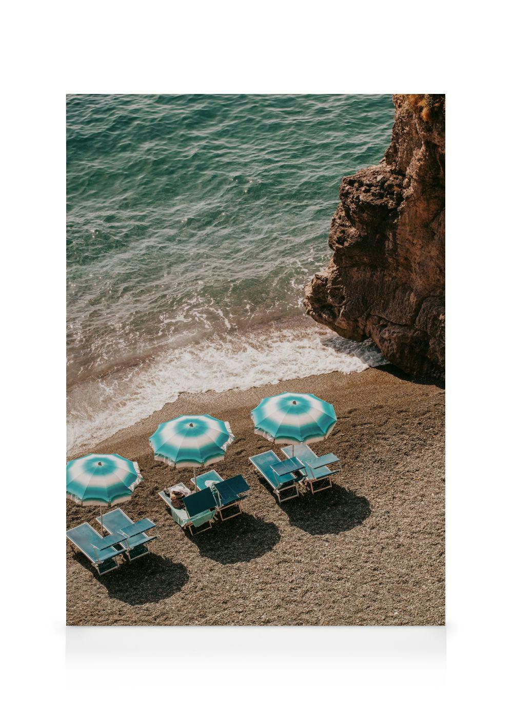 Leinwandbild einer malerischen Bucht mit türkisfarbenem Meer, Kieselstrand, Felsen und Sonnenschirmen.