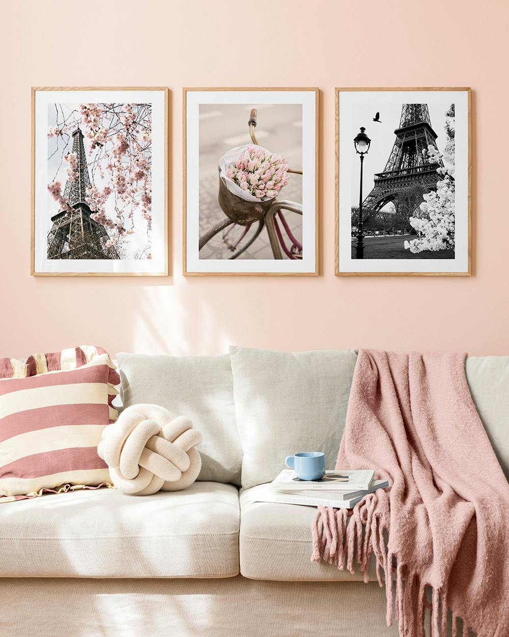 Postersets met Eiffeltoren en fiets met tulpen, hangend boven een bank in een roze kamer.