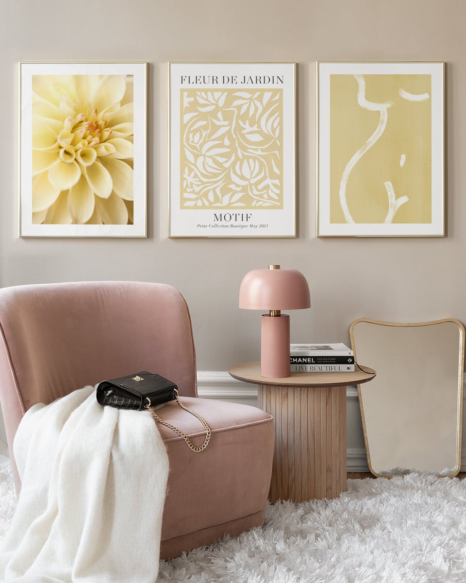 Tre lyse, gule plakater på en bildevegg i en moderne stue med rosa stol og bord.