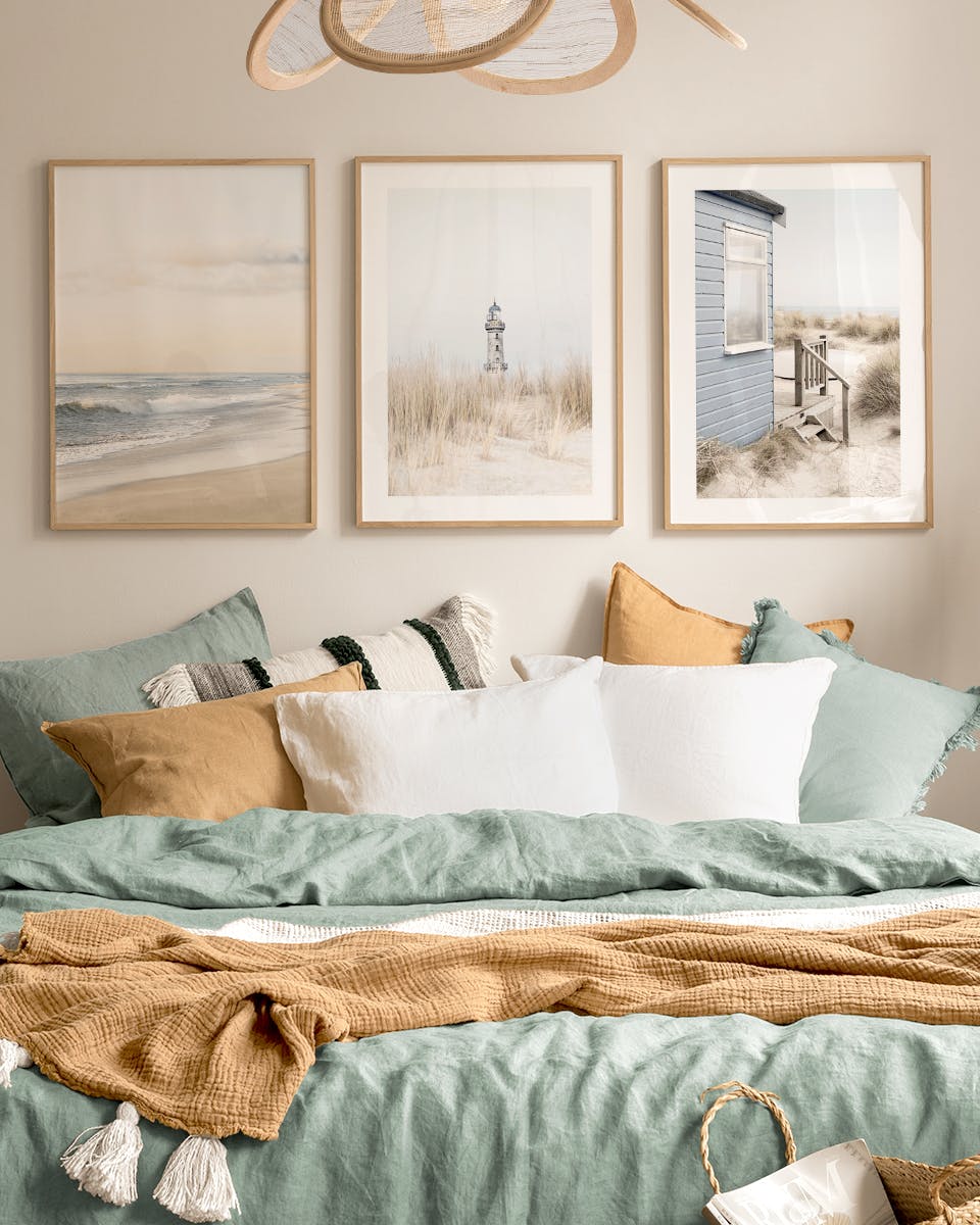 Bilderwand mit drei Küstenmotiven: Strand, Leuchtturm und Strandhaus, über einem Bett mit mintgrüner und senfgelber Bettwäsche.