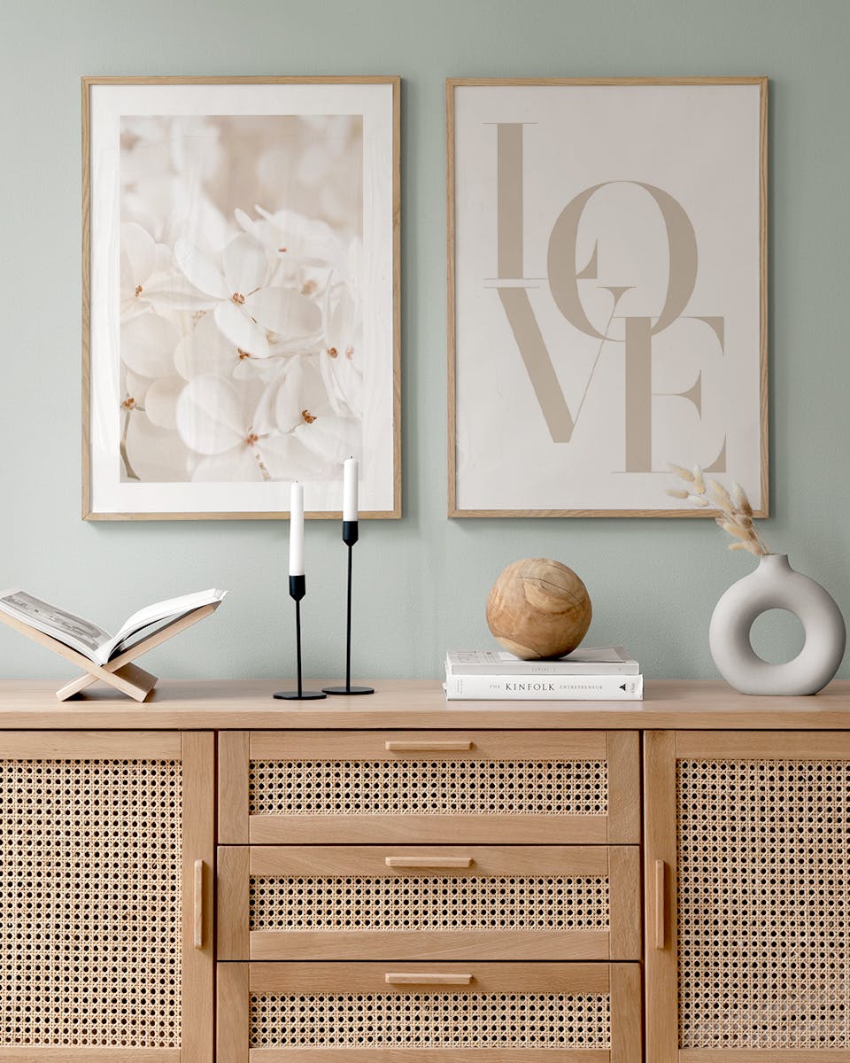 A poster pack displayed above a rattan wood sideboard, showing a white floral print and a beige LOVE typographic print.