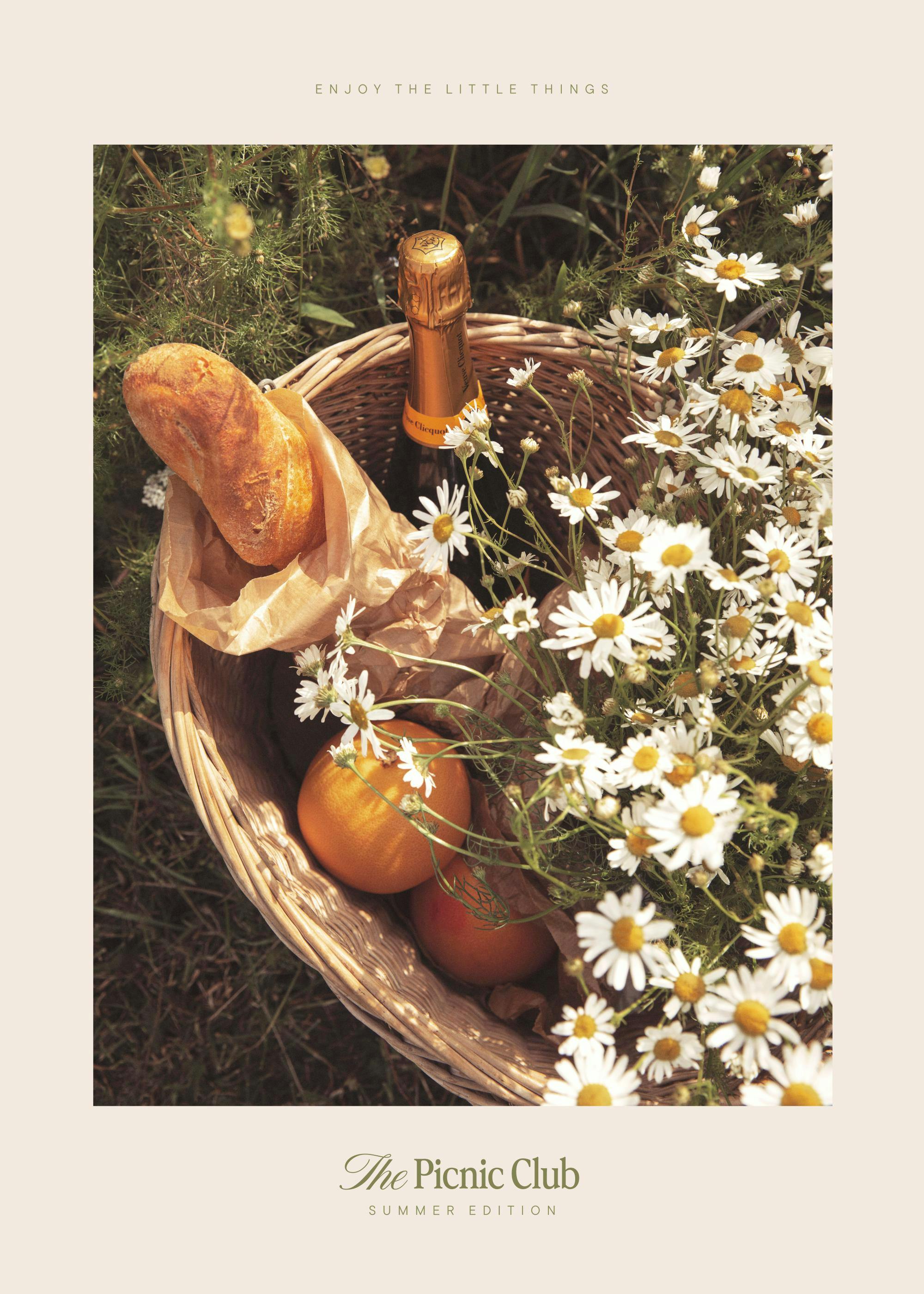 A poster featuring a picnic basket filled with champagne, bread, fruit, and daisies, surrounded by green foliage.