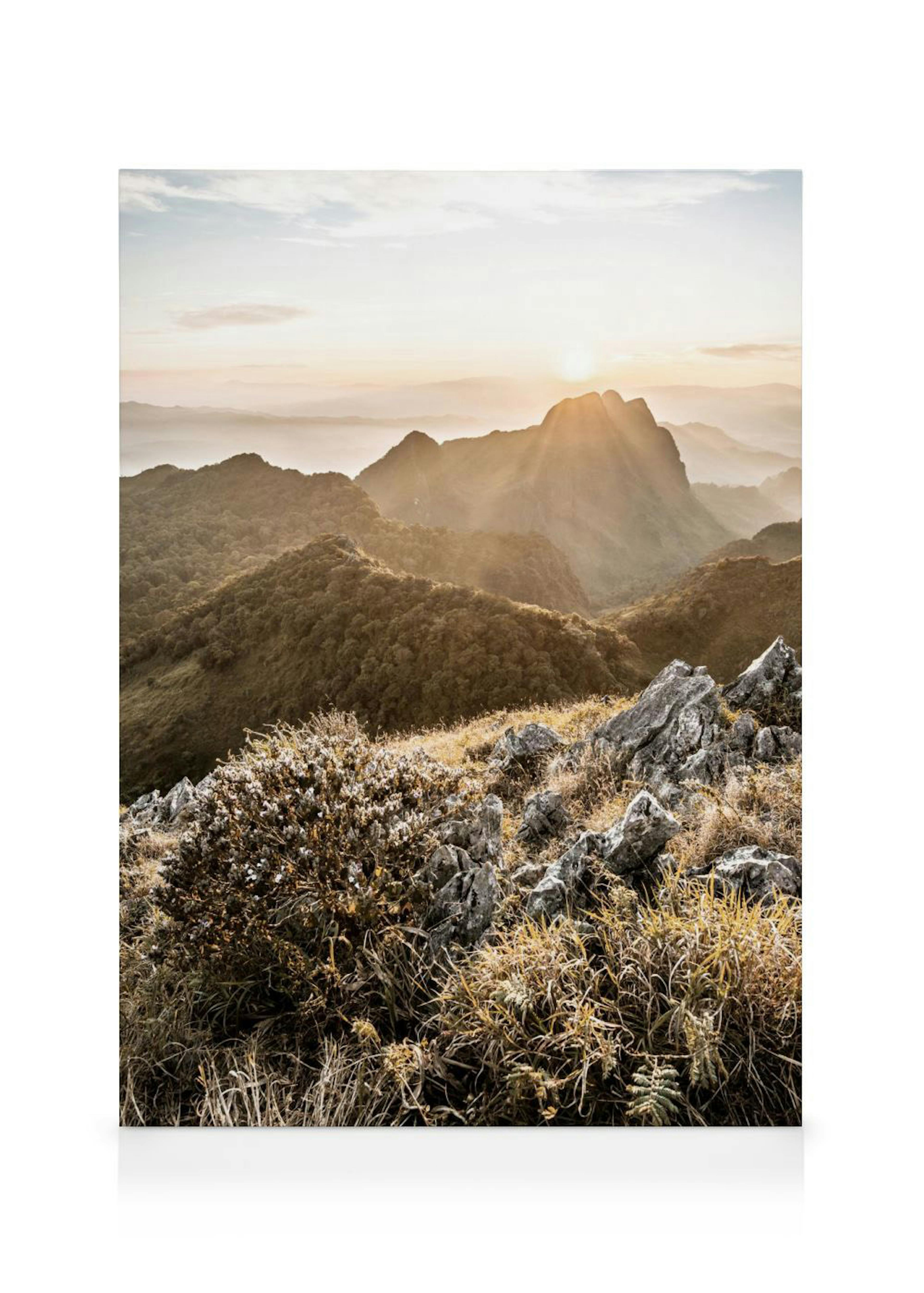 A canvas displaying a mountain landscape with sun rays breaking through the peak at sunrise, with rocks and dry grass in the for