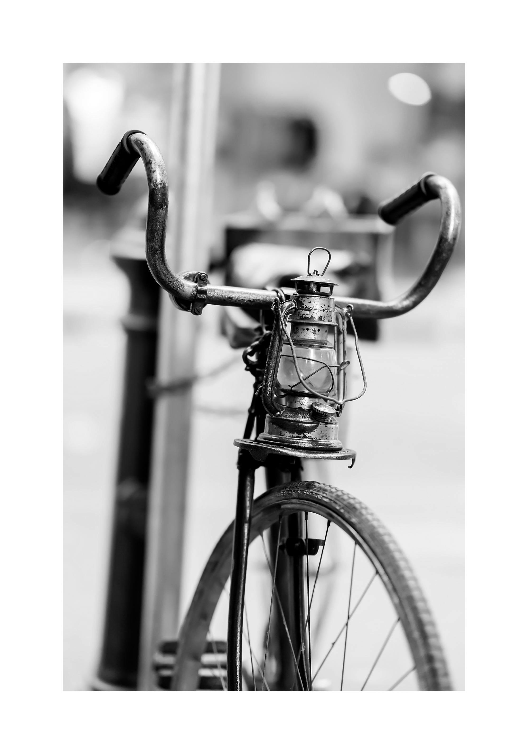 Plakat przedstawiający czarno-białe zdjęcie starego roweru z lampą na kierownicy, na pierwszym planie.
