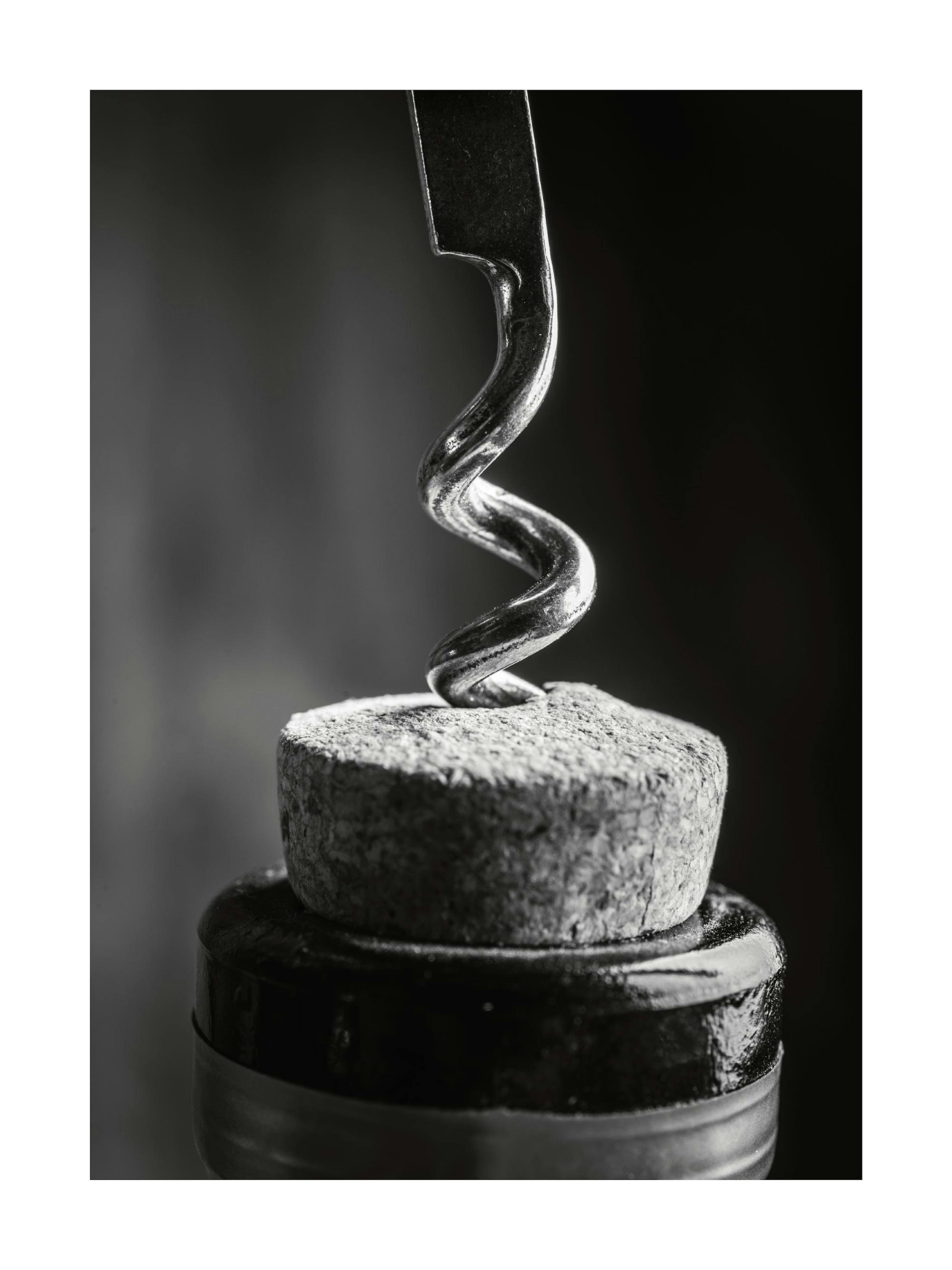 A black and white poster showing a metallic corkscrew inserted into a cork on top of a wine bottle.
