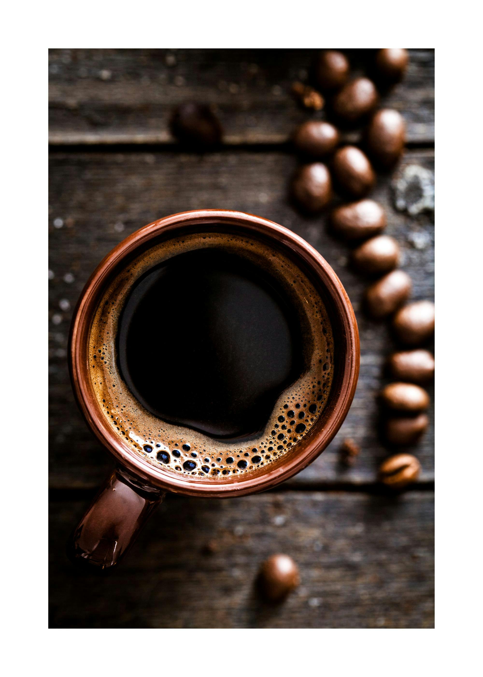 Een poster van een kopje zwarte koffie met schuim, omringd door koffiebonen op een houten tafel.