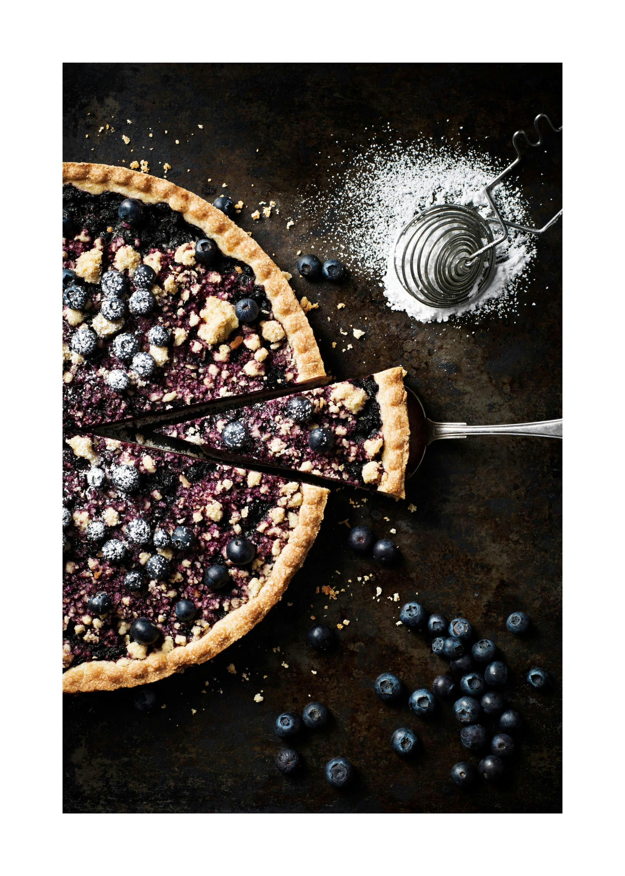 A poster featuring a blueberry crumble pie with a slice being removed, alongside loose blueberries and powdered sugar.