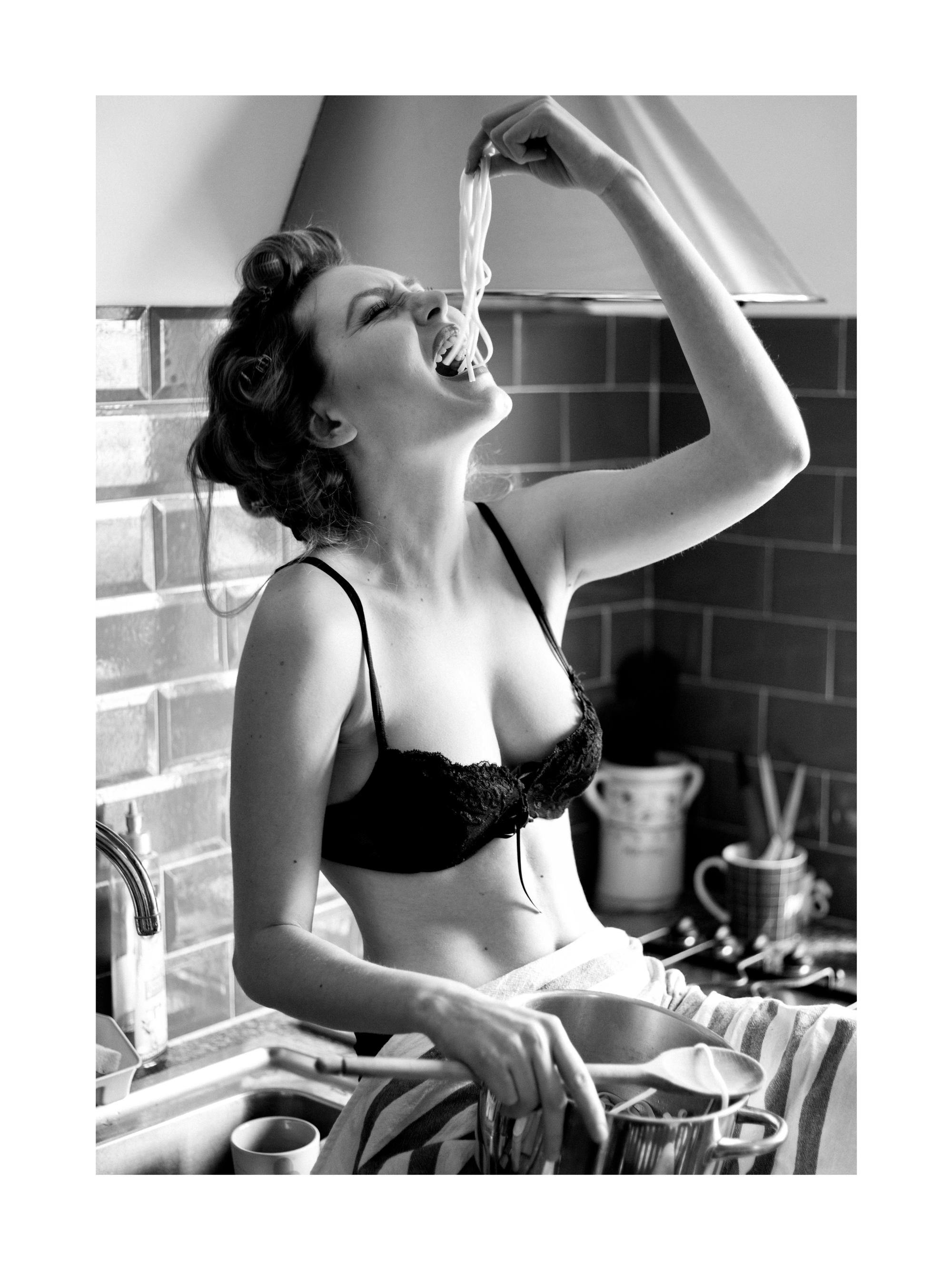 Un poster alb-negru cu o femeie în bucătărie, mâncând spaghete dintr-o oală.