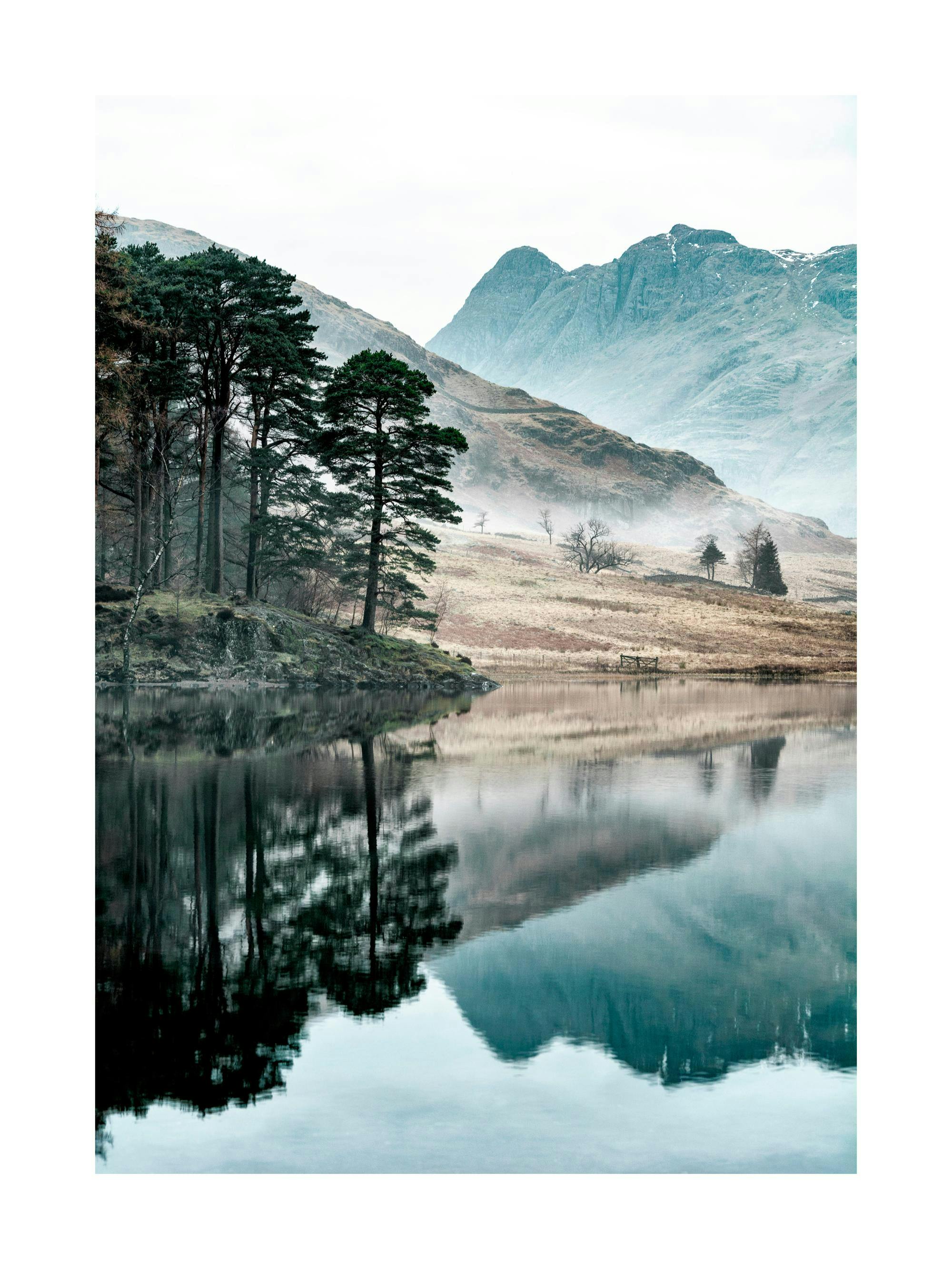 Un poster di un lago calmo che riflette pini e montagne maestose, con nebbia sottile e cielo chiaro.