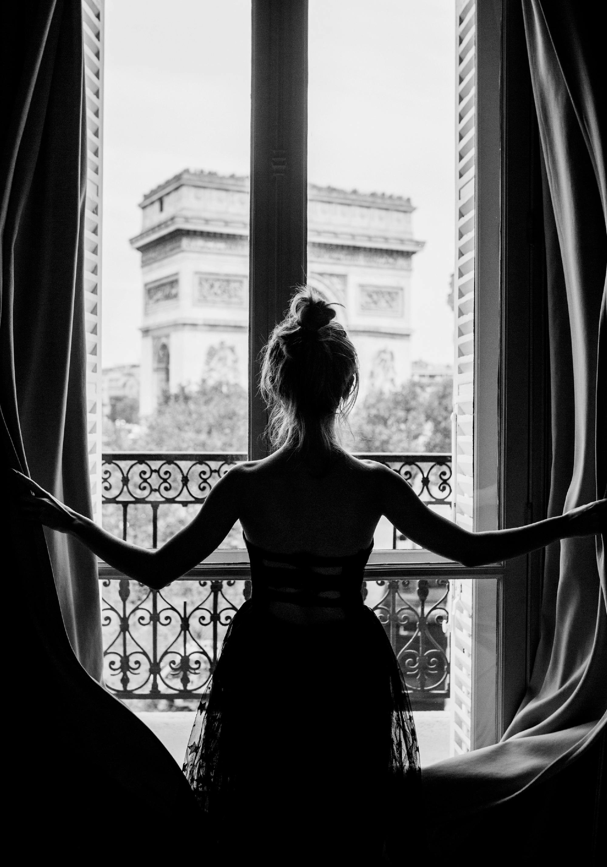 Zwart-witte poster van een vrouw die uit het raam kijkt naar de Arc de Triomphe in Parijs.