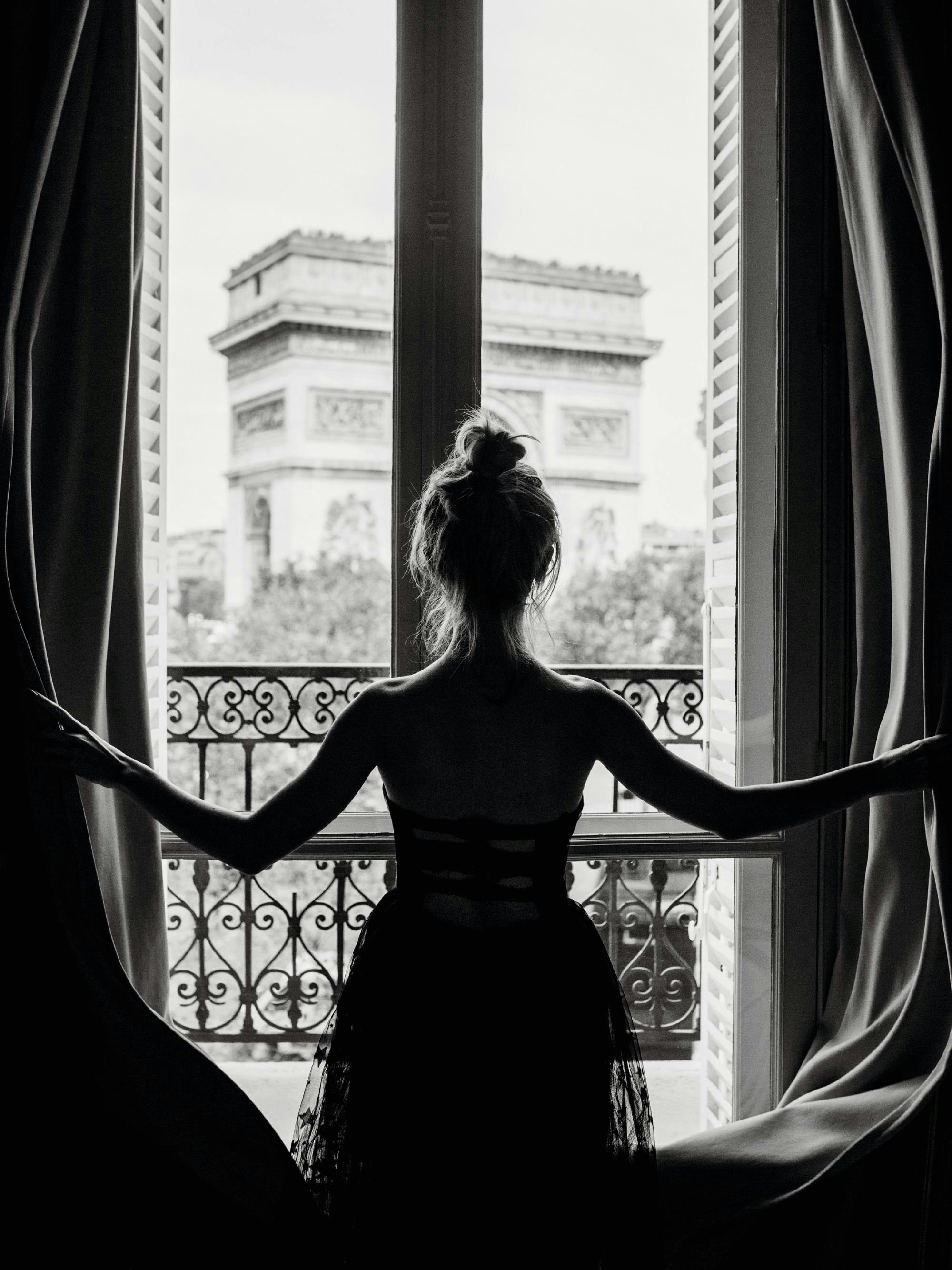 A black and white poster of a woman silhouetted against a window, looking out at the Arc de Triomphe.