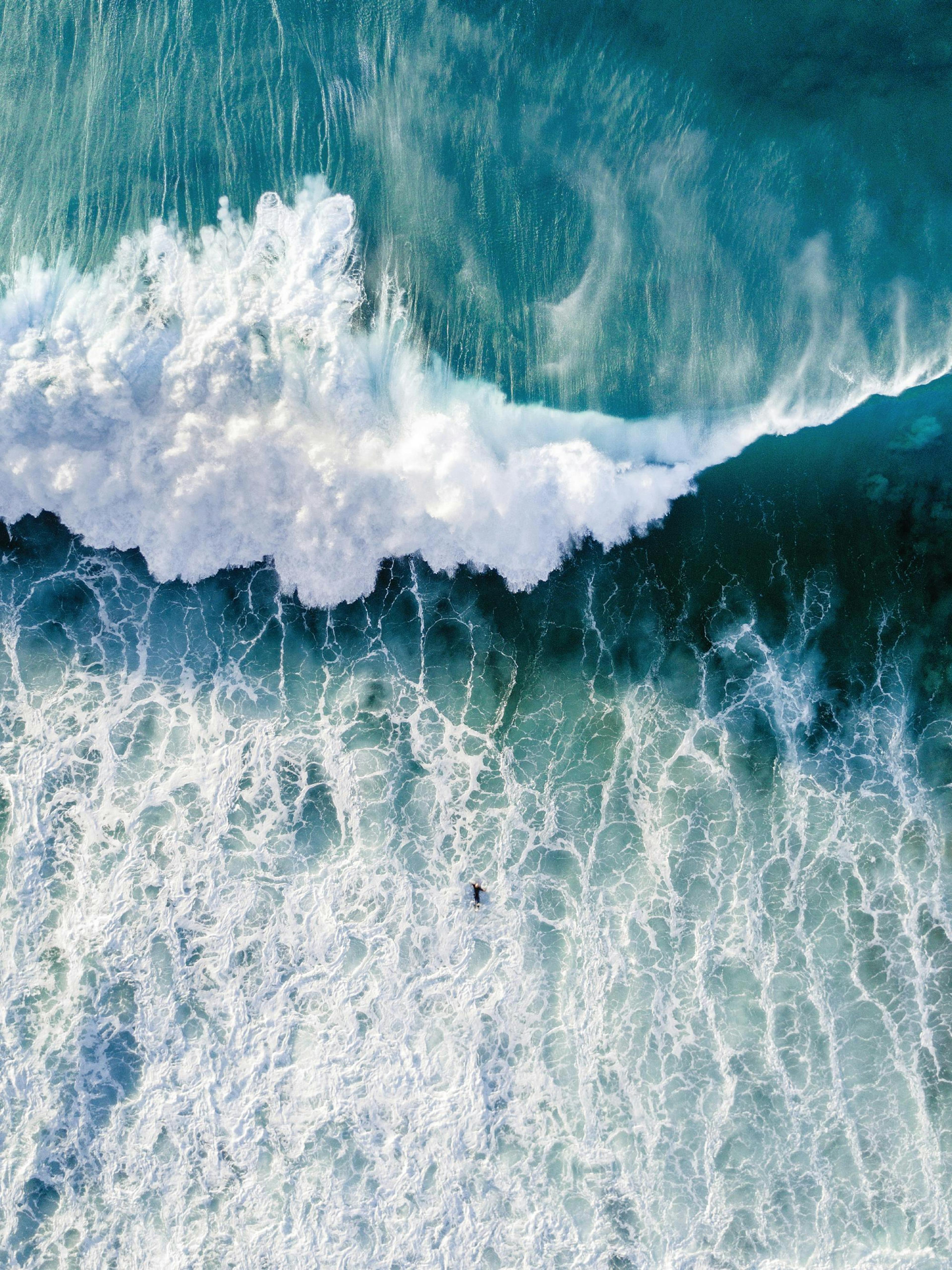 Póster de una vista aérea de una ola oceánica rompiendo, con agua turquesa y espuma blanca, y un surfista.