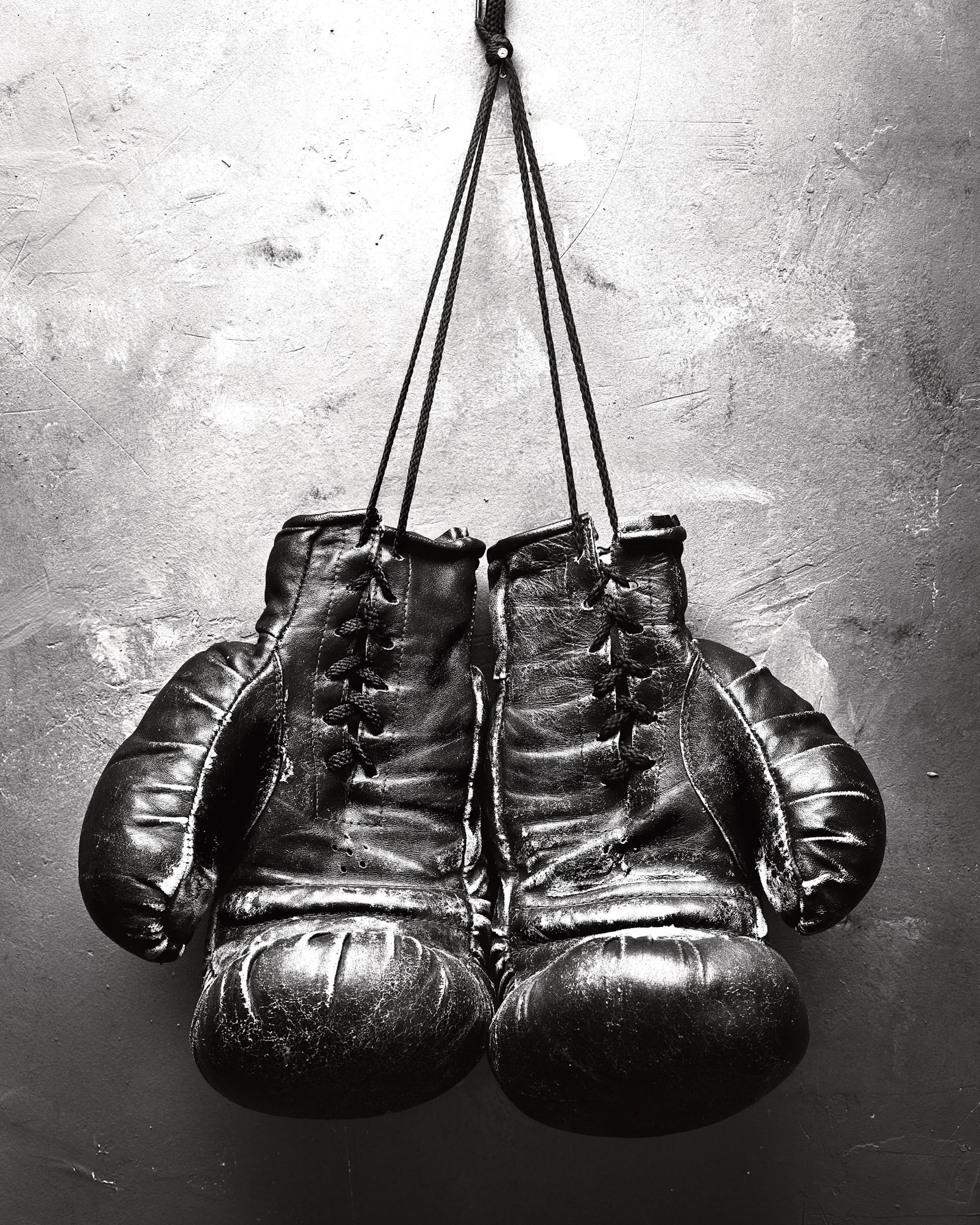 A black and white poster of old, worn boxing gloves hanging by their laces against a textured wall.