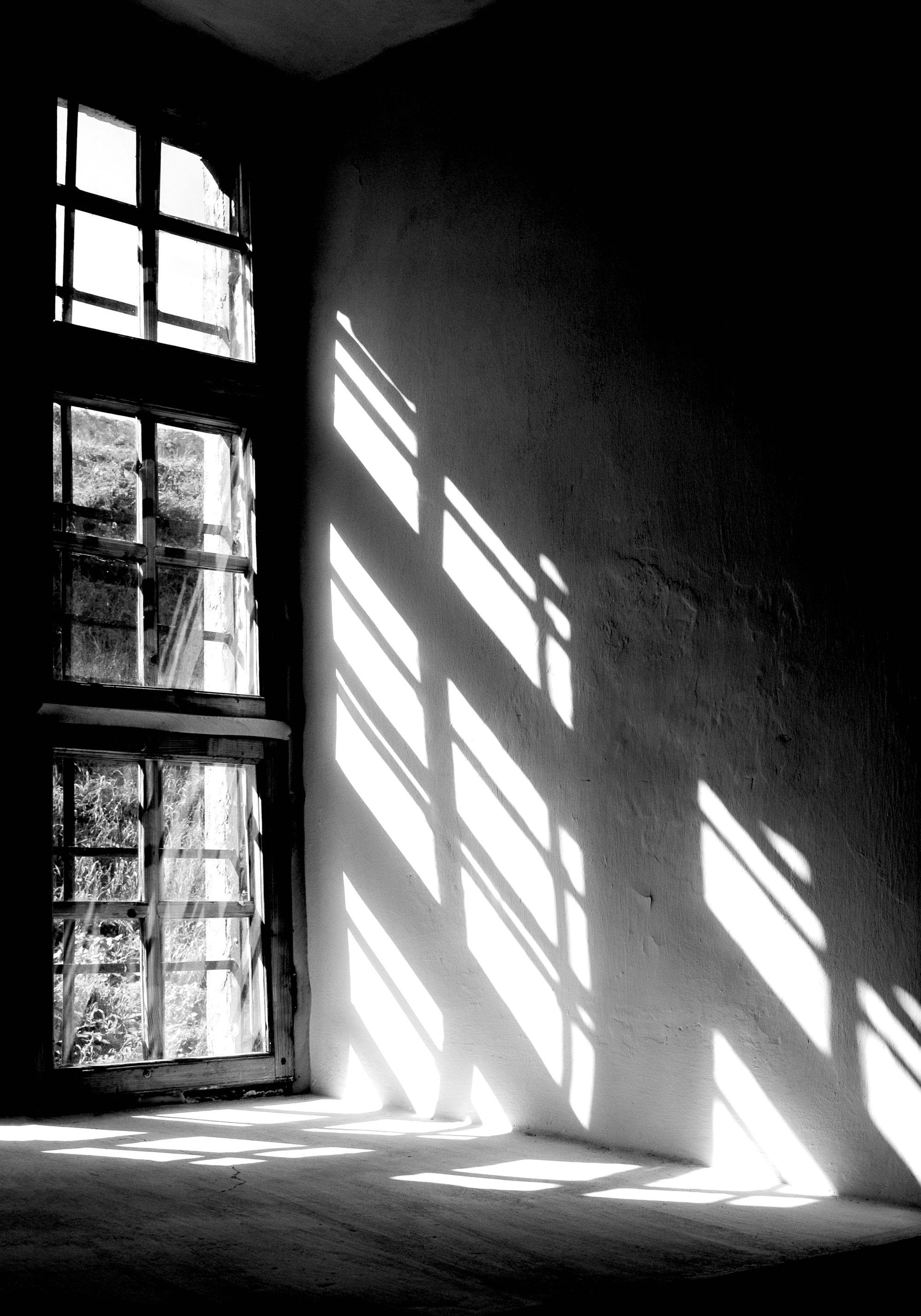 A black and white poster showing sunlight casting strong rectangular shadows from a window onto a textured wall and floor.