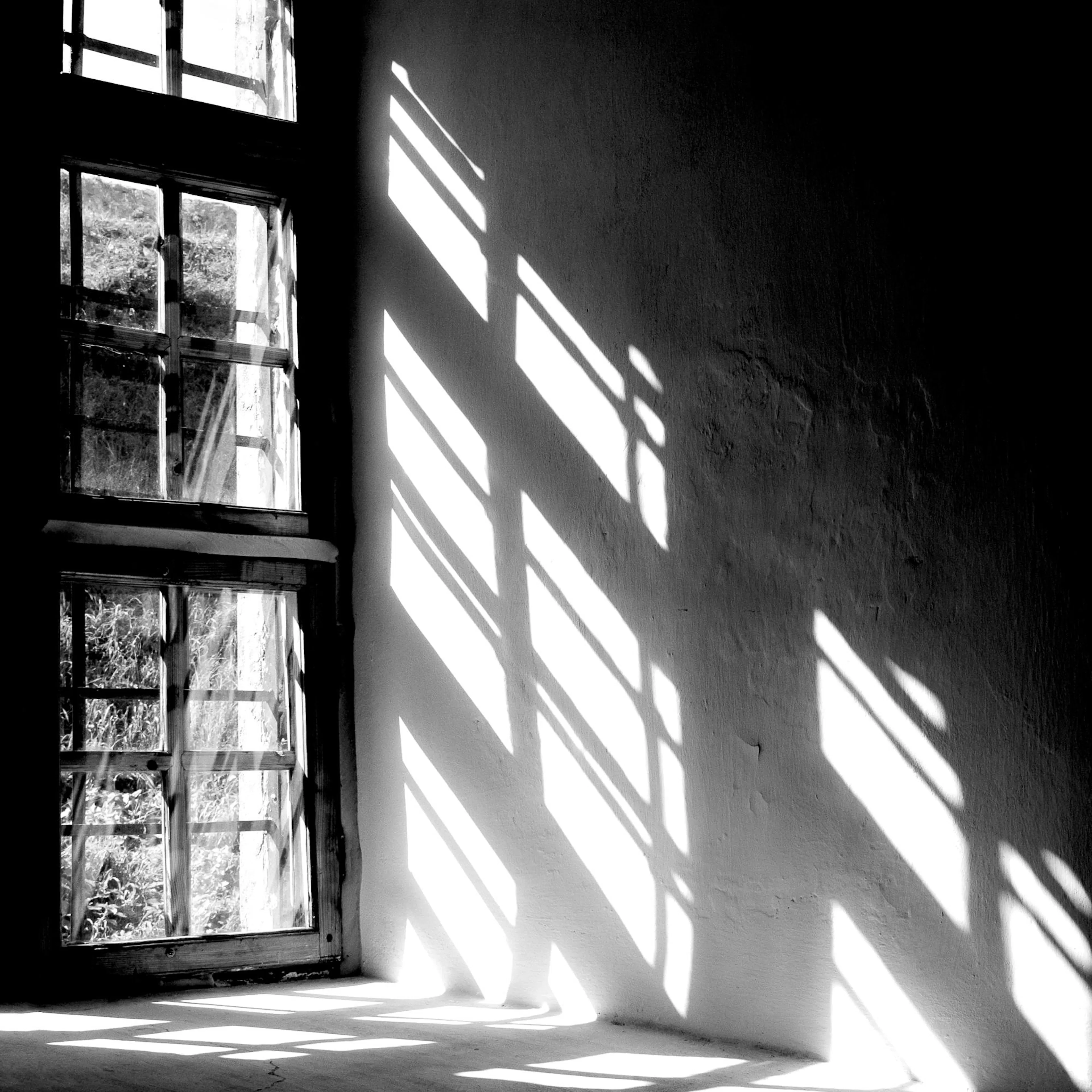 Un poster en noir et blanc dune fenêtre à carreaux projetant des motifs lumineux sur un mur et le sol.