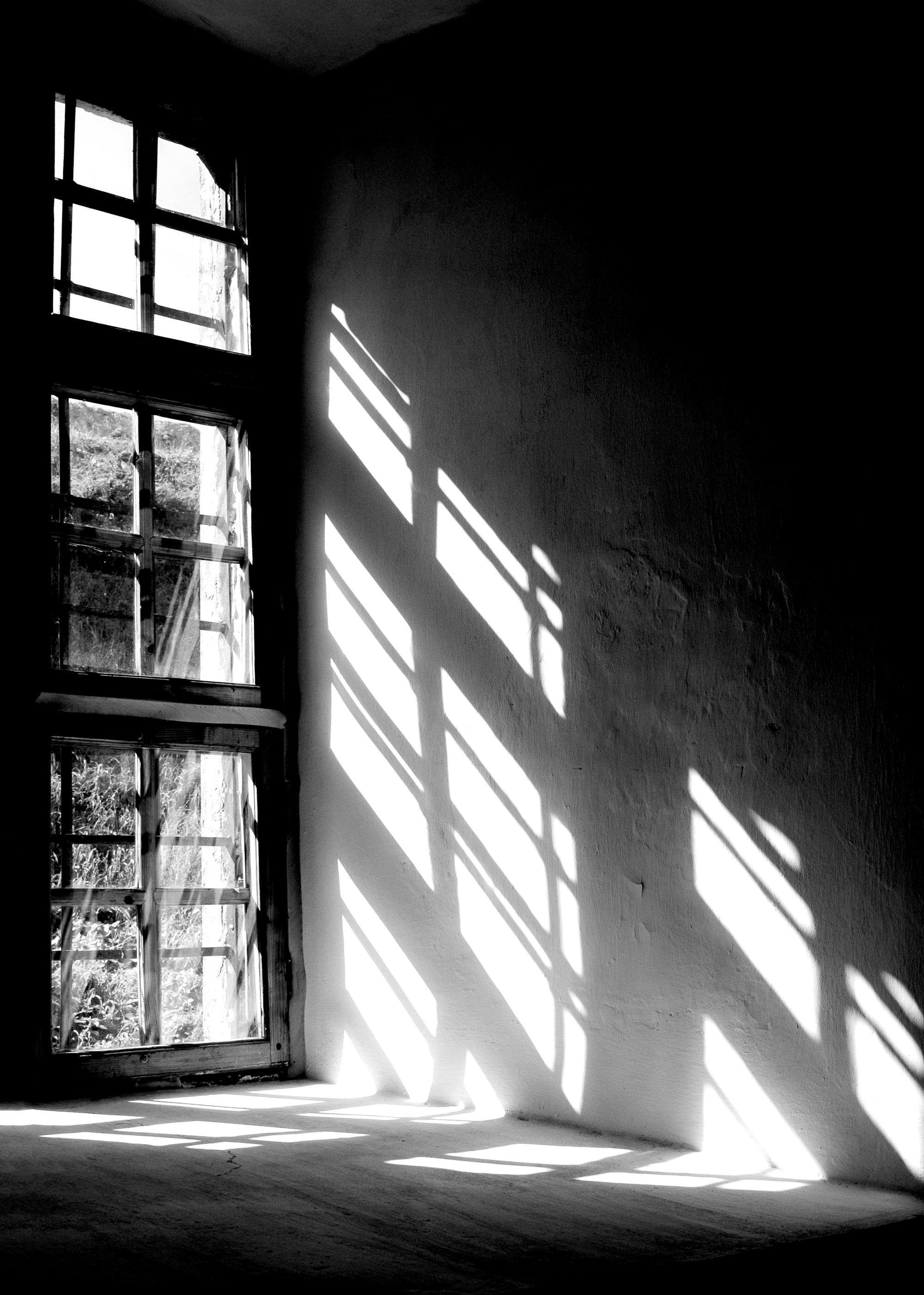 A black and white poster of a window casting grid shadows on a textured wall and floor.
