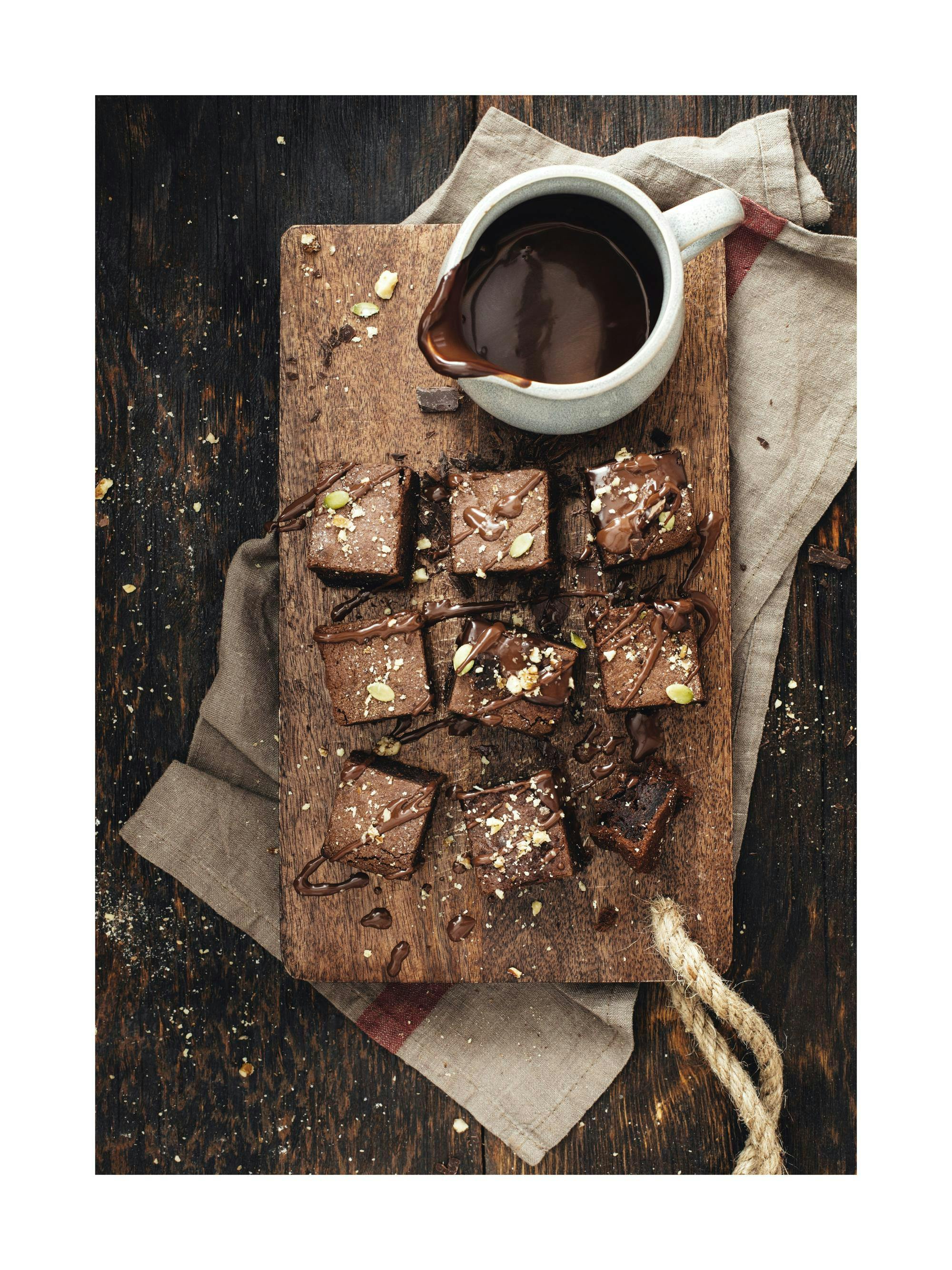 A delicious poster of chocolate brownies with nuts and seeds, drizzled with chocolate sauce, on a wooden board.