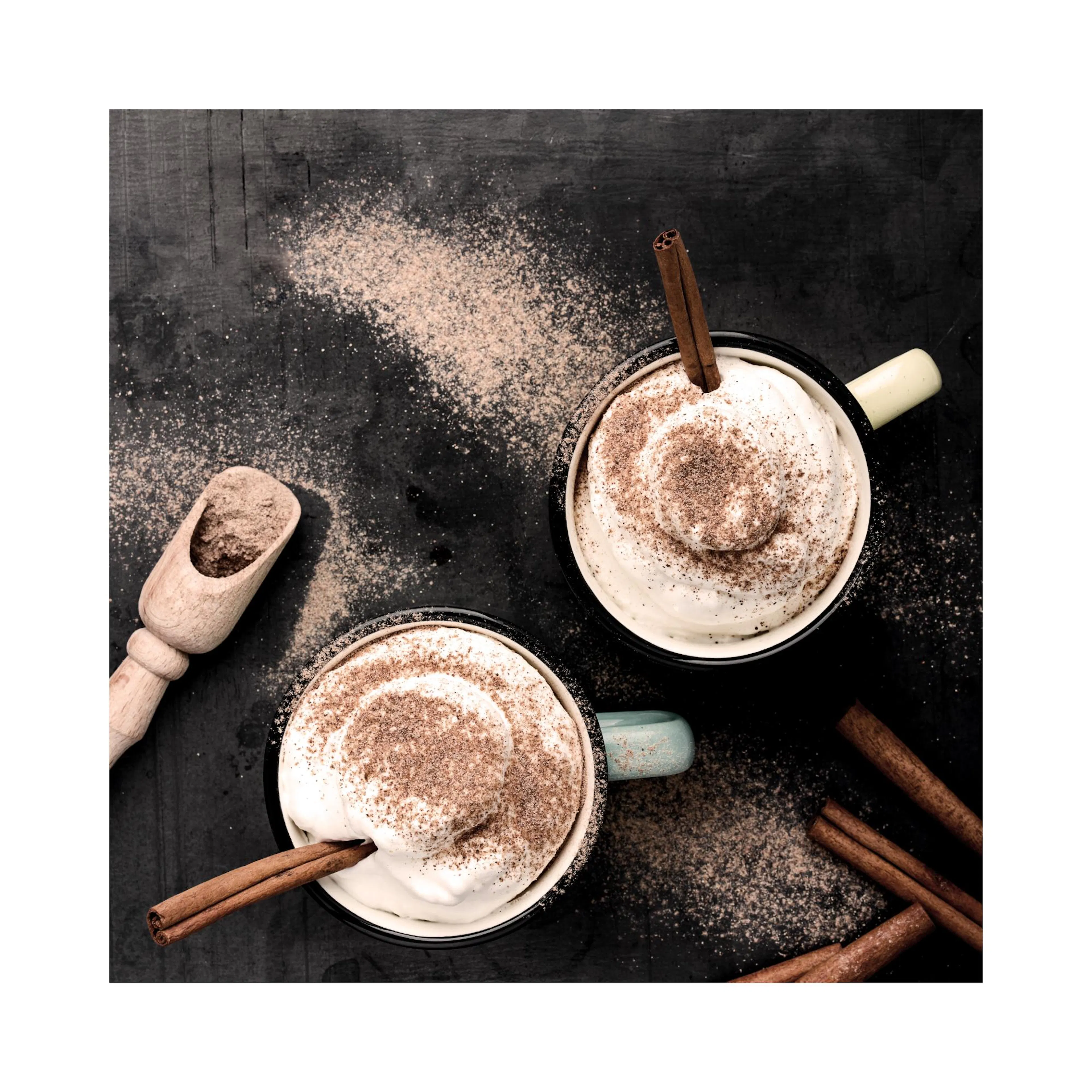 Póster de dos tazas de chocolate caliente con crema batida, canela en rama y cacao en polvo sobre una mesa oscura.