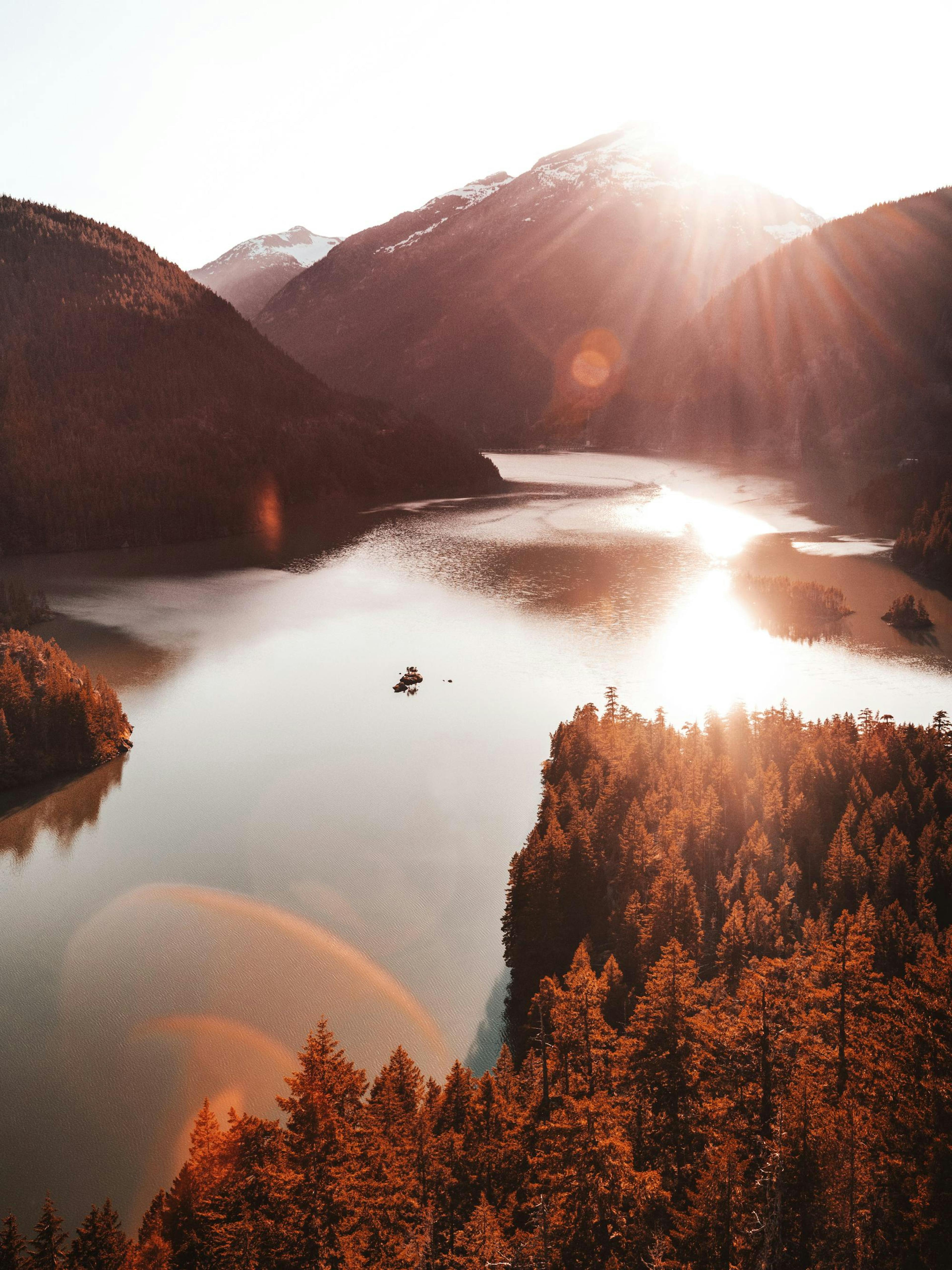 A poster of a vast lake nestled between dark mountains and evergreen forests, with a bright sunburst reflecting on the water.