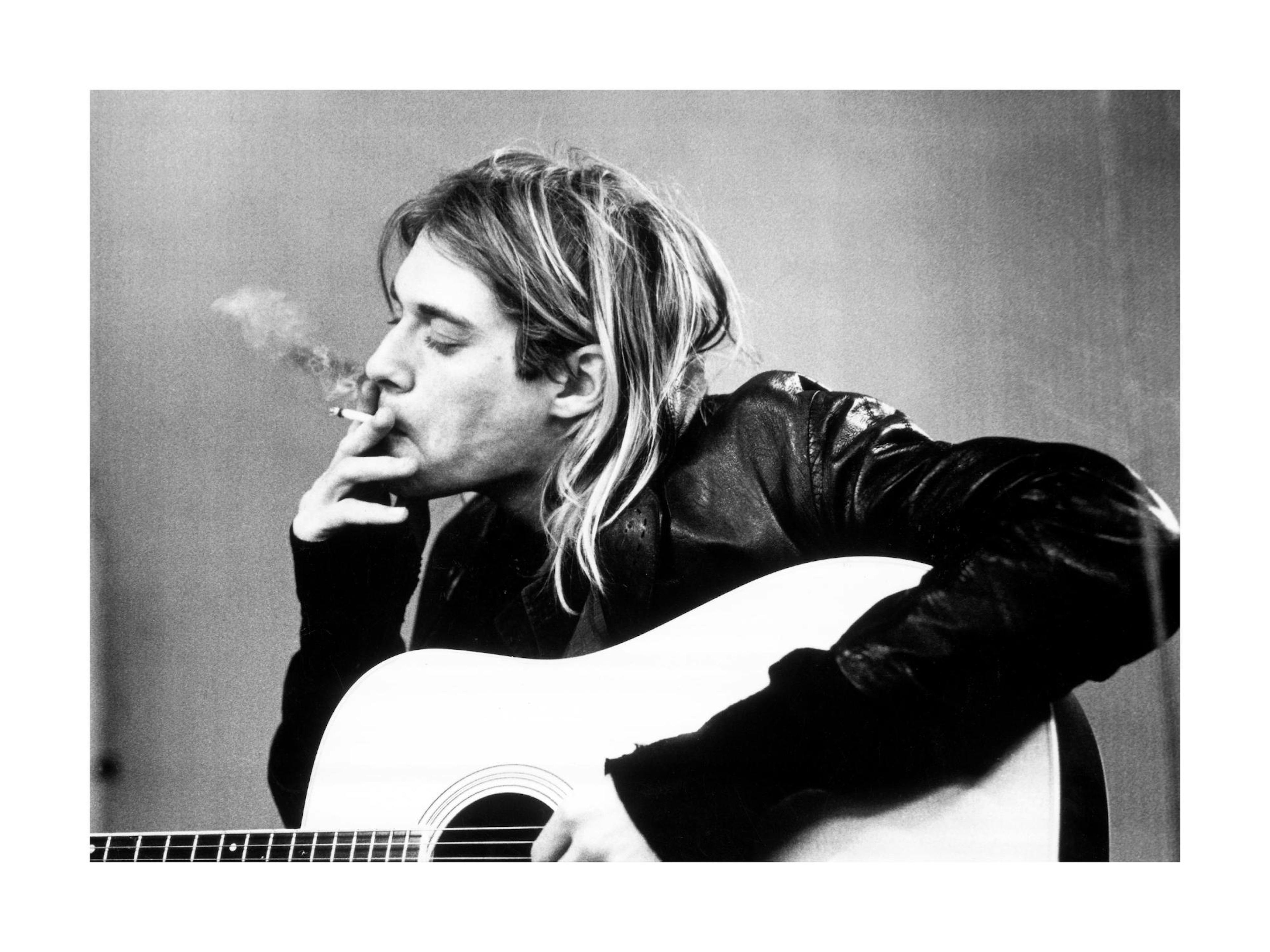A black and white poster of Kurt Cobain with long blonde hair, wearing a leather jacket and smoking a cigarette while holding an