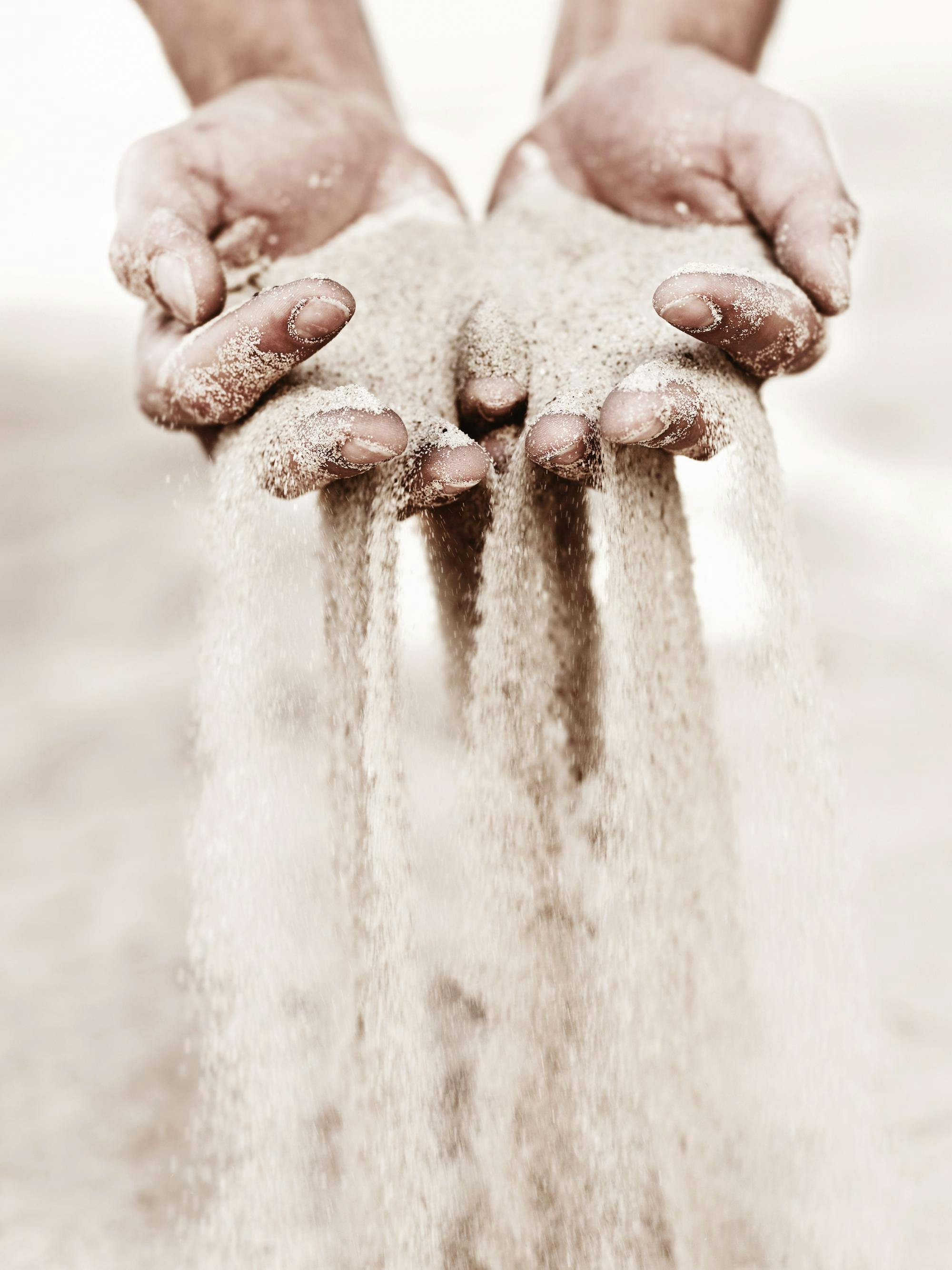 A sepia-toned poster showing hands cupped together, letting light-coloured sand pour through the fingers.