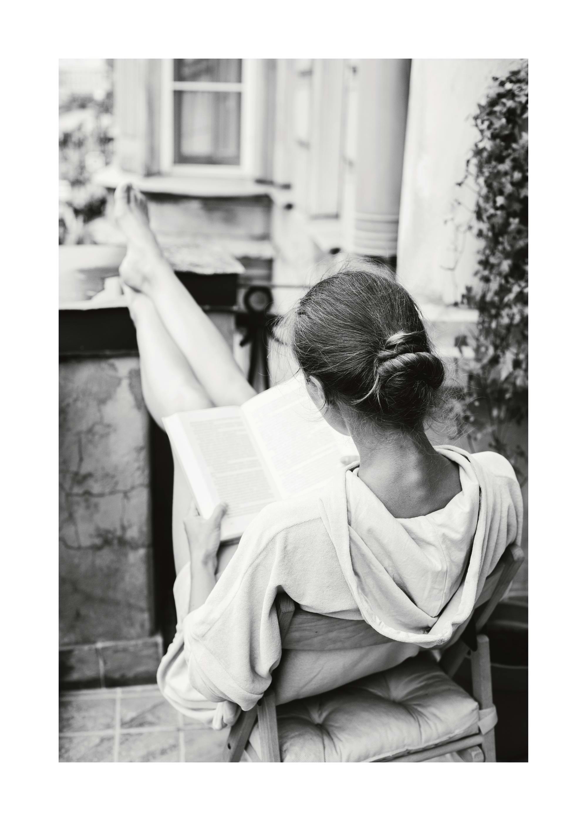 A black and white poster of a person reading a book with their feet up, relaxing outdoors.