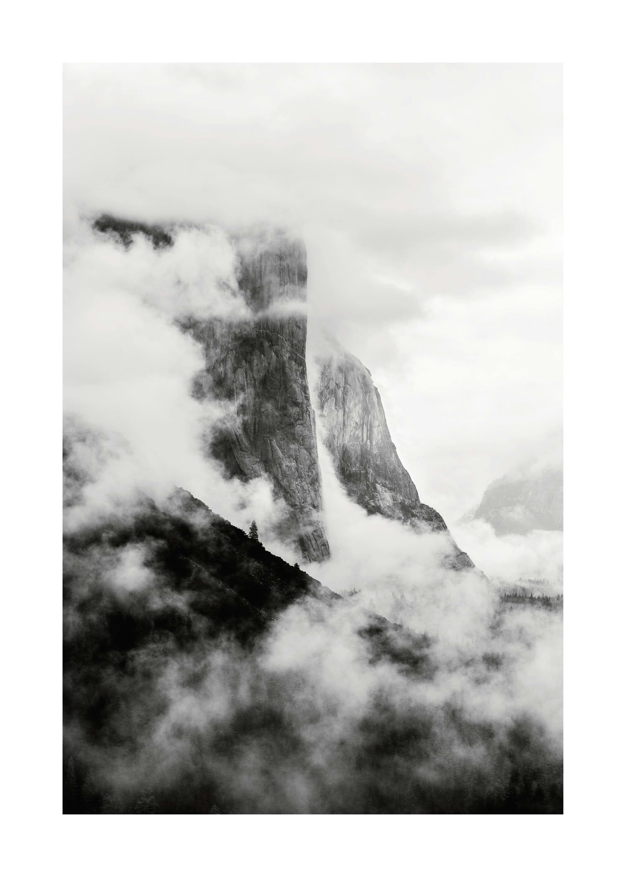 Zwart-wit poster van een berg omgeven door mist en wolken, met donkere bosrijke hellingen op de voorgrond.