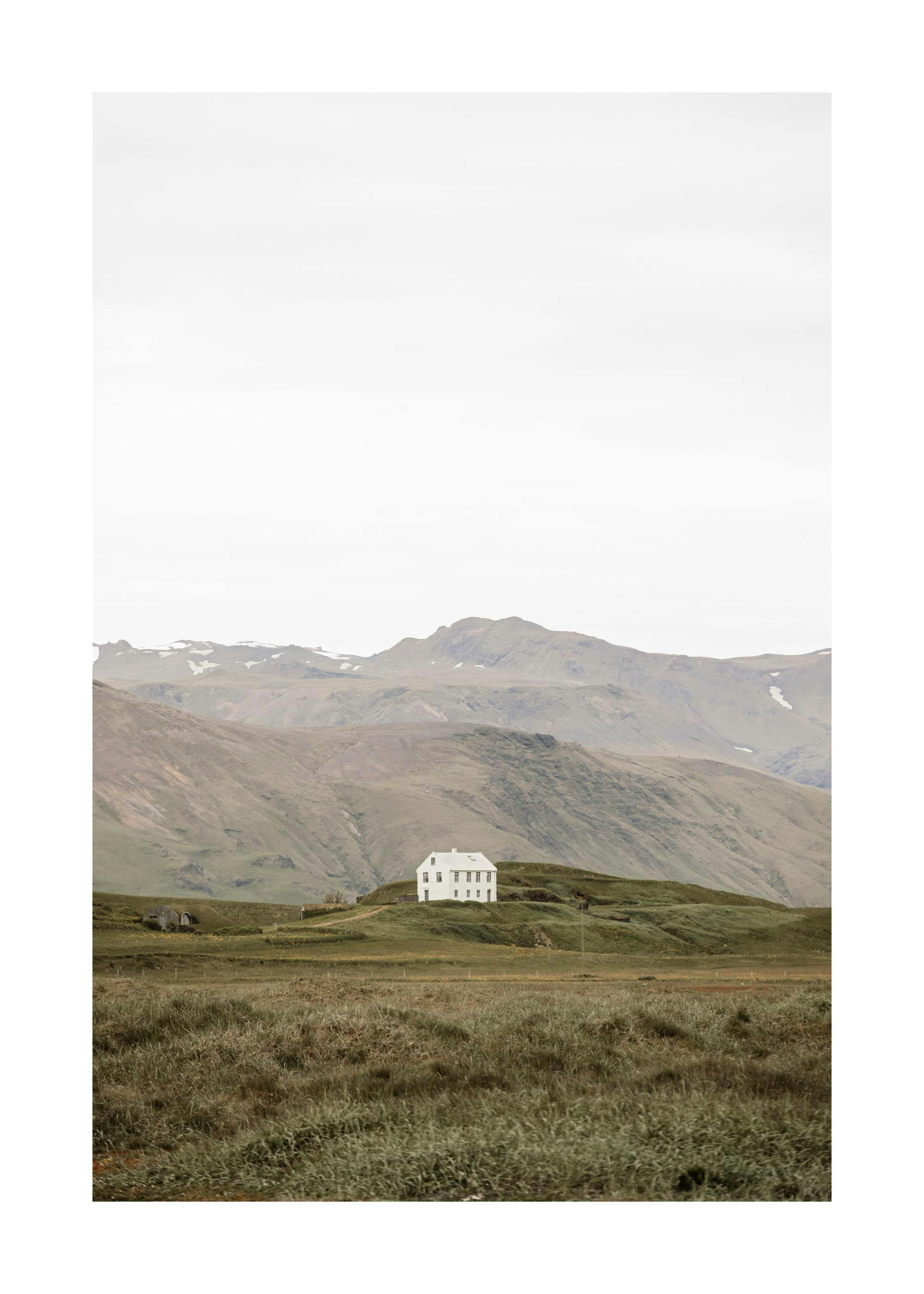 A poster featuring a white house on a green hill with mountains in the background, under a bright sky.