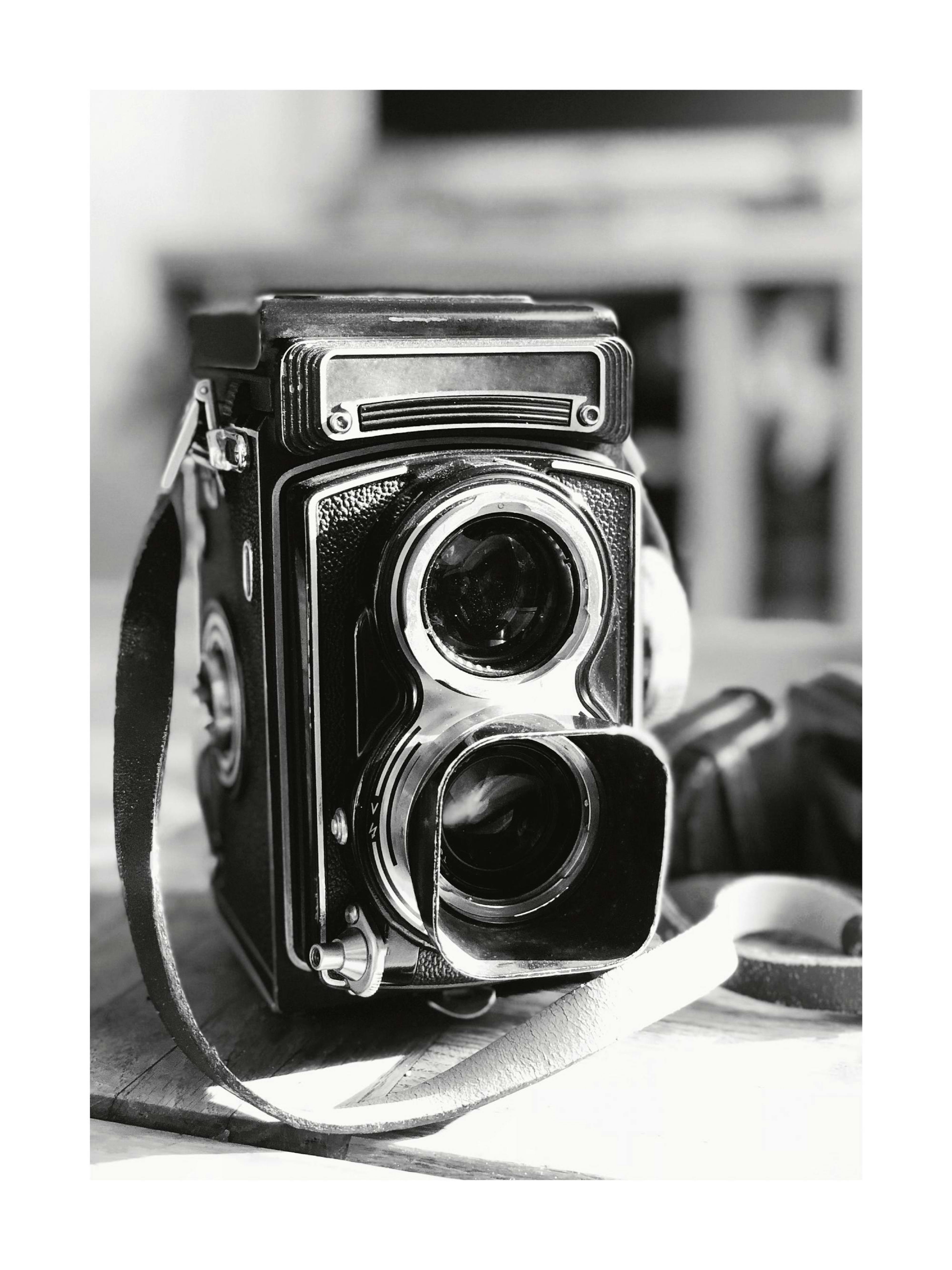 A black and white poster featuring a vintage twin-lens reflex camera with a leather strap on a wooden surface.