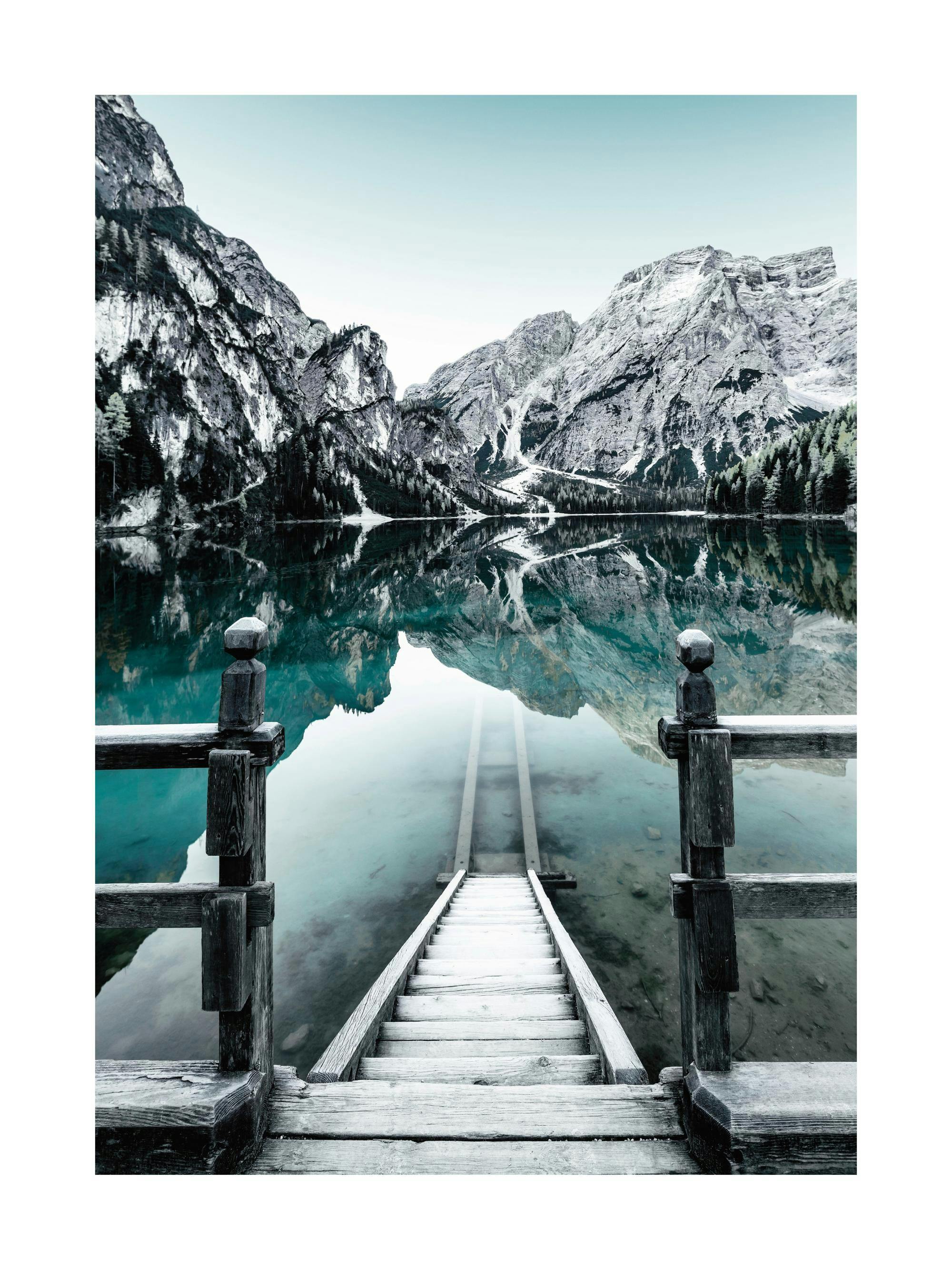 A poster featuring a wooden jetty and steps leading into a serene lake, reflecting snow-capped mountains and a pale blue sky.