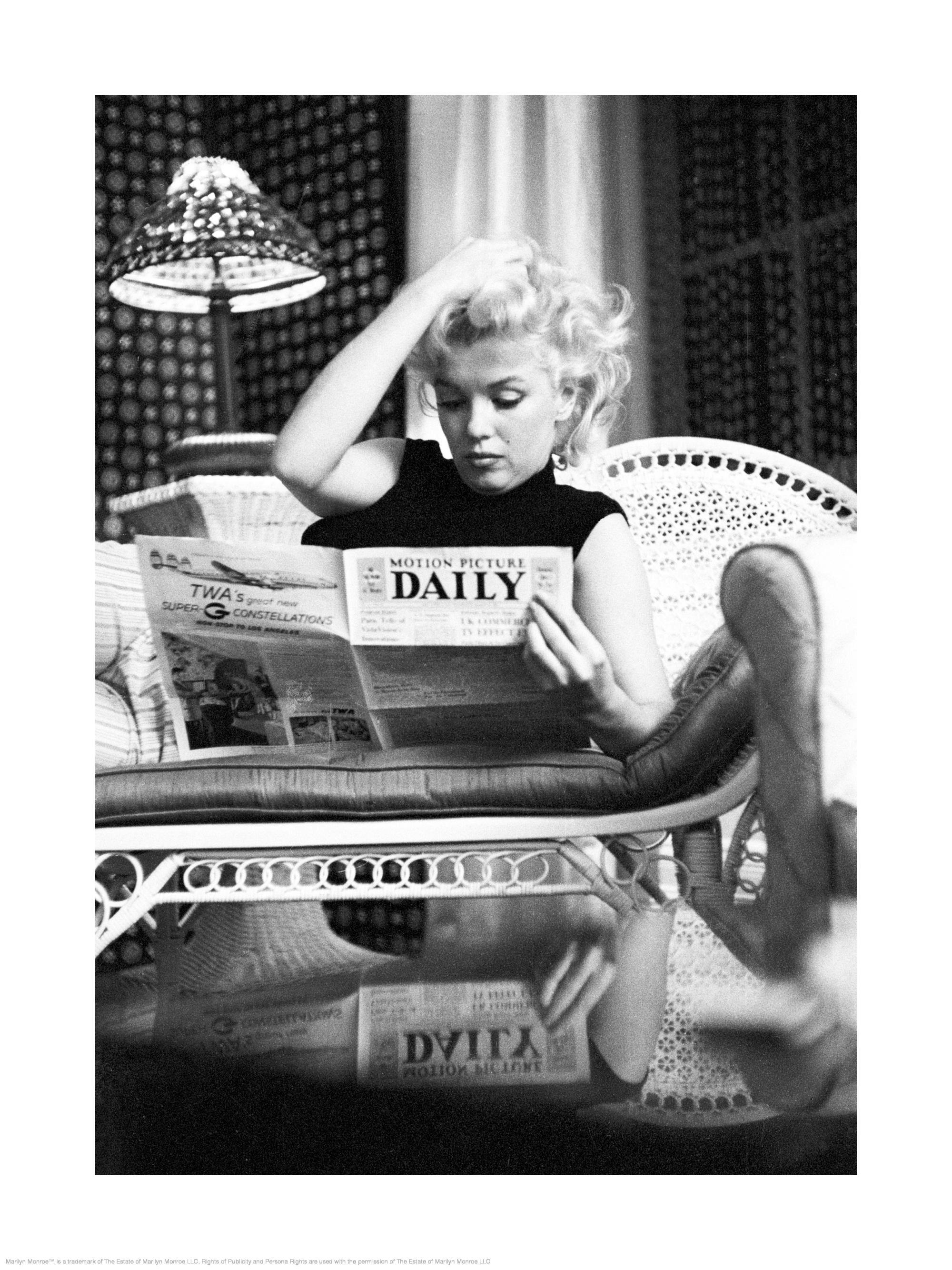 Zwart-wit poster van Marilyn Monroe die haar haar aanraakt terwijl ze een krant leest in een rieten stoel.