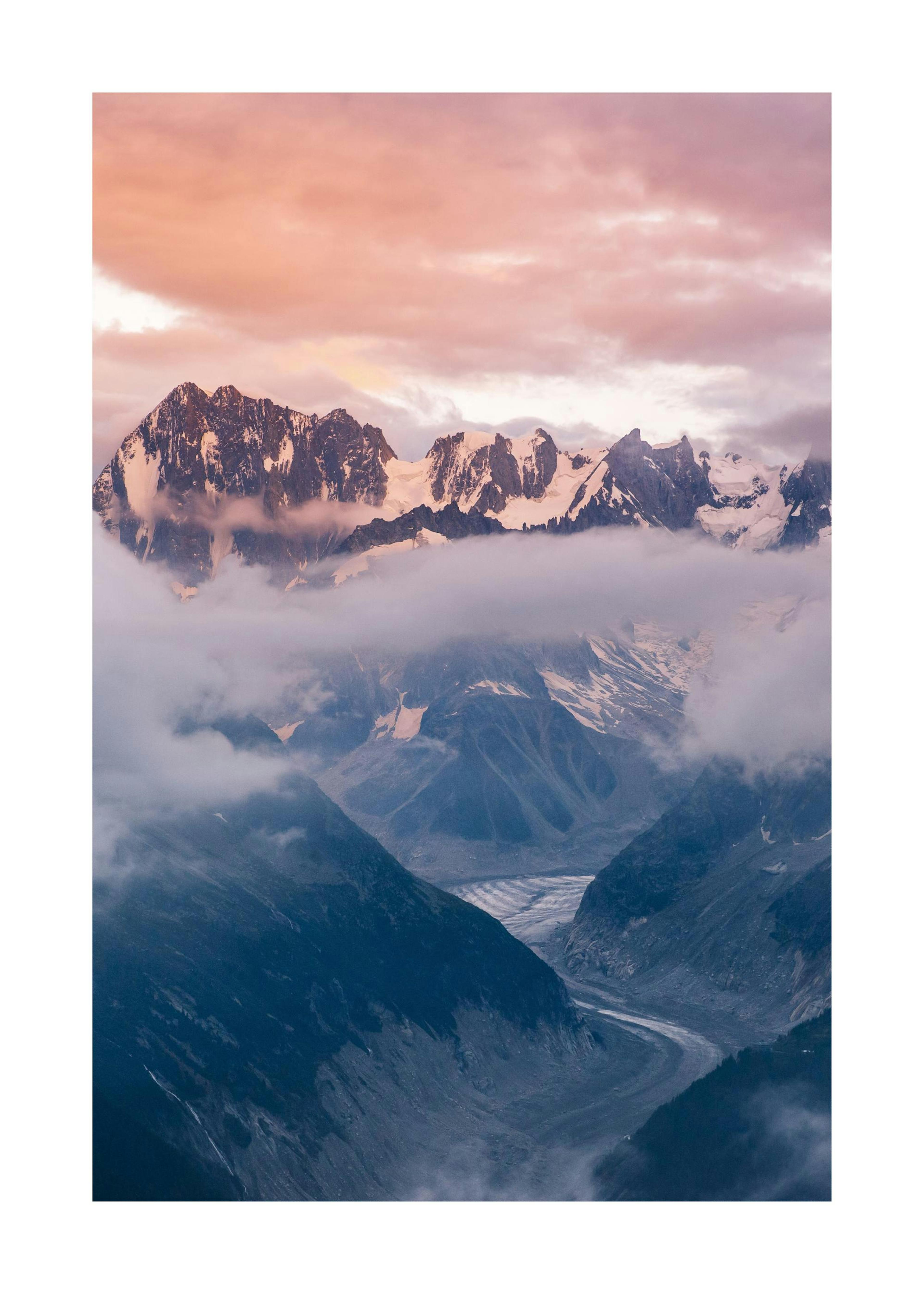 A poster featuring a dramatic mountain landscape with pink clouds and a winding glacier, hanging above a bedside table with a la