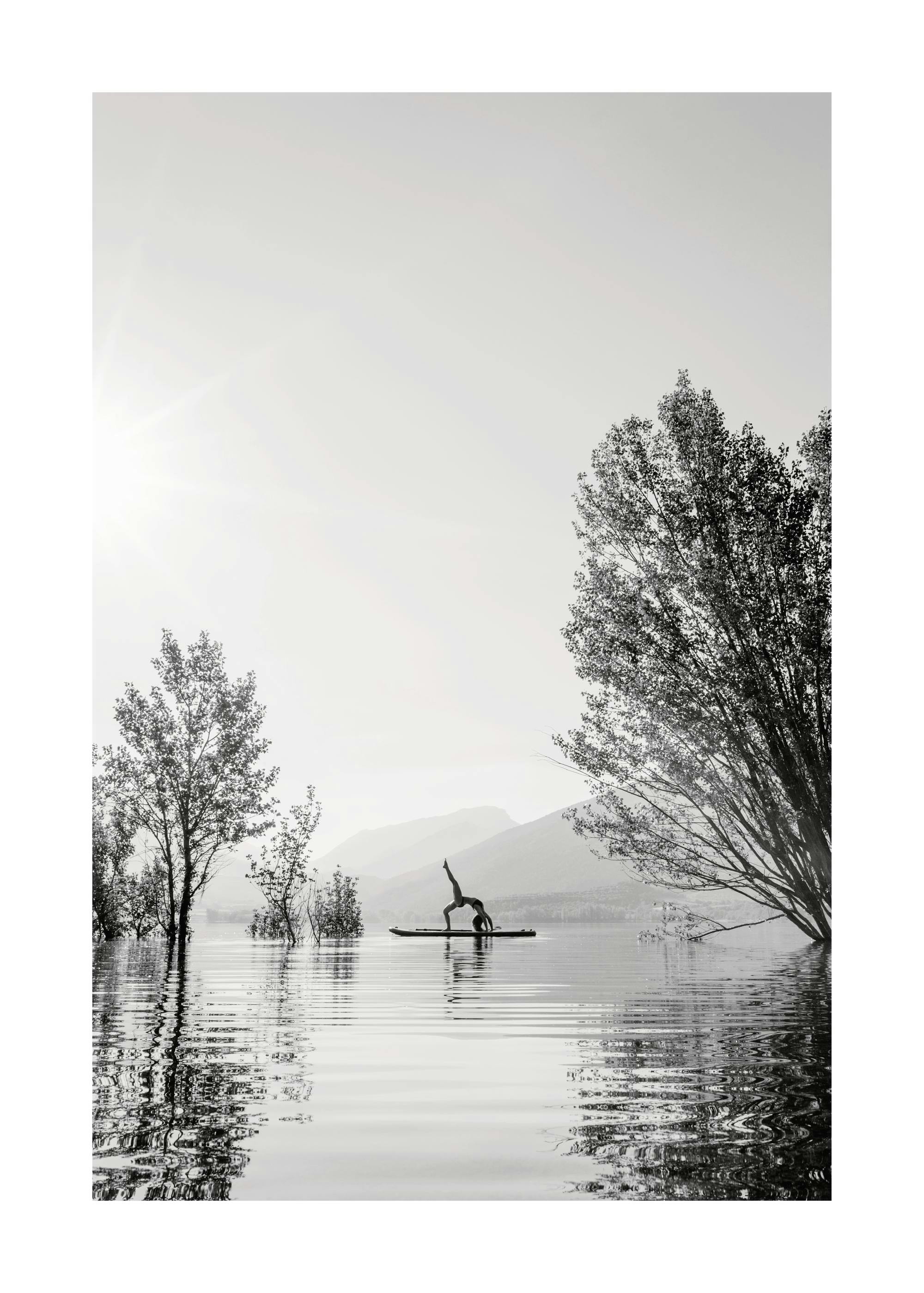 A poster of a person silhouetted doing yoga on a paddleboard in a lake, with trees and mountains in the background.