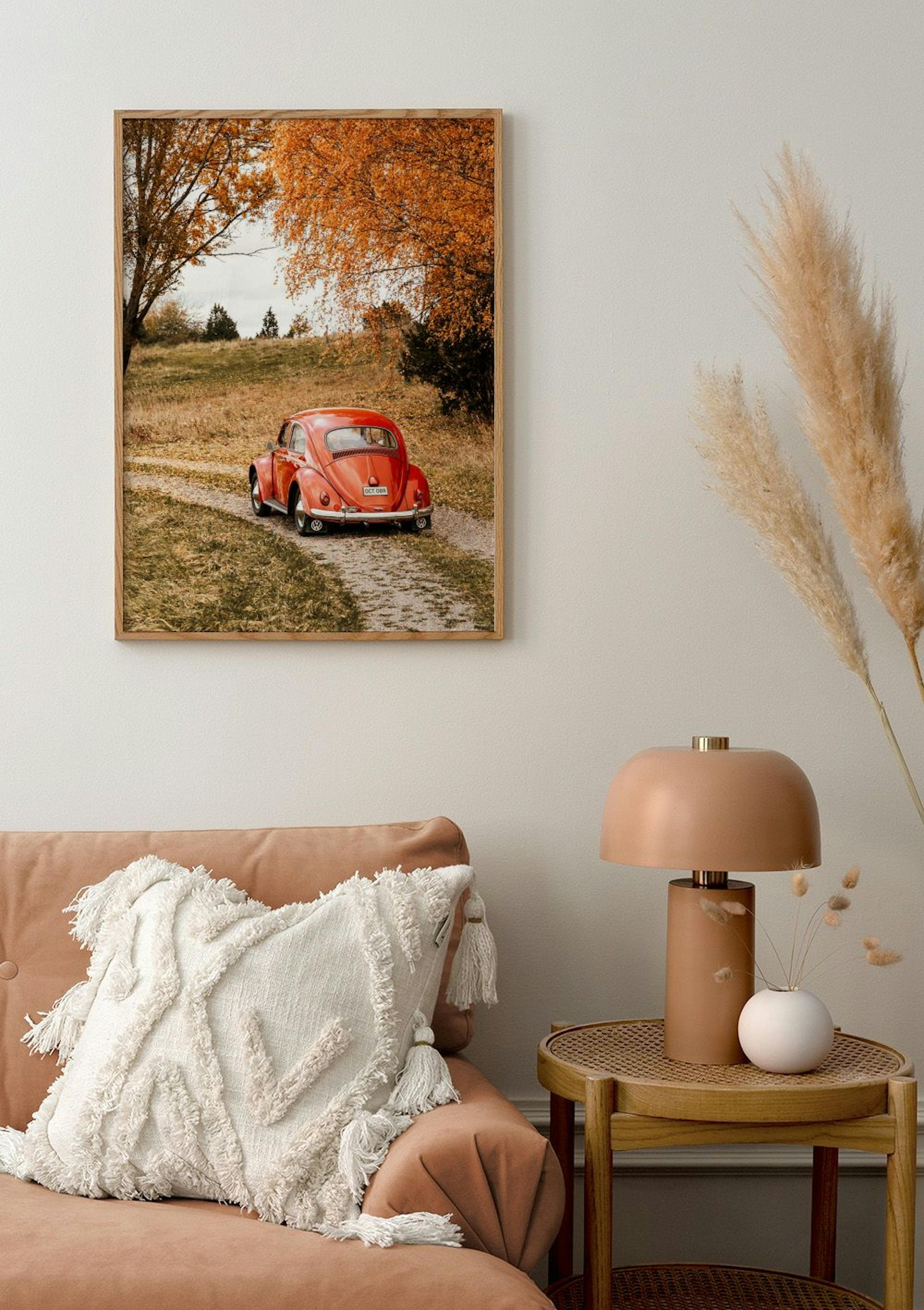 A poster of a red vintage car on a dirt road, surrounded by autumn trees, hanging above a peach sofa.