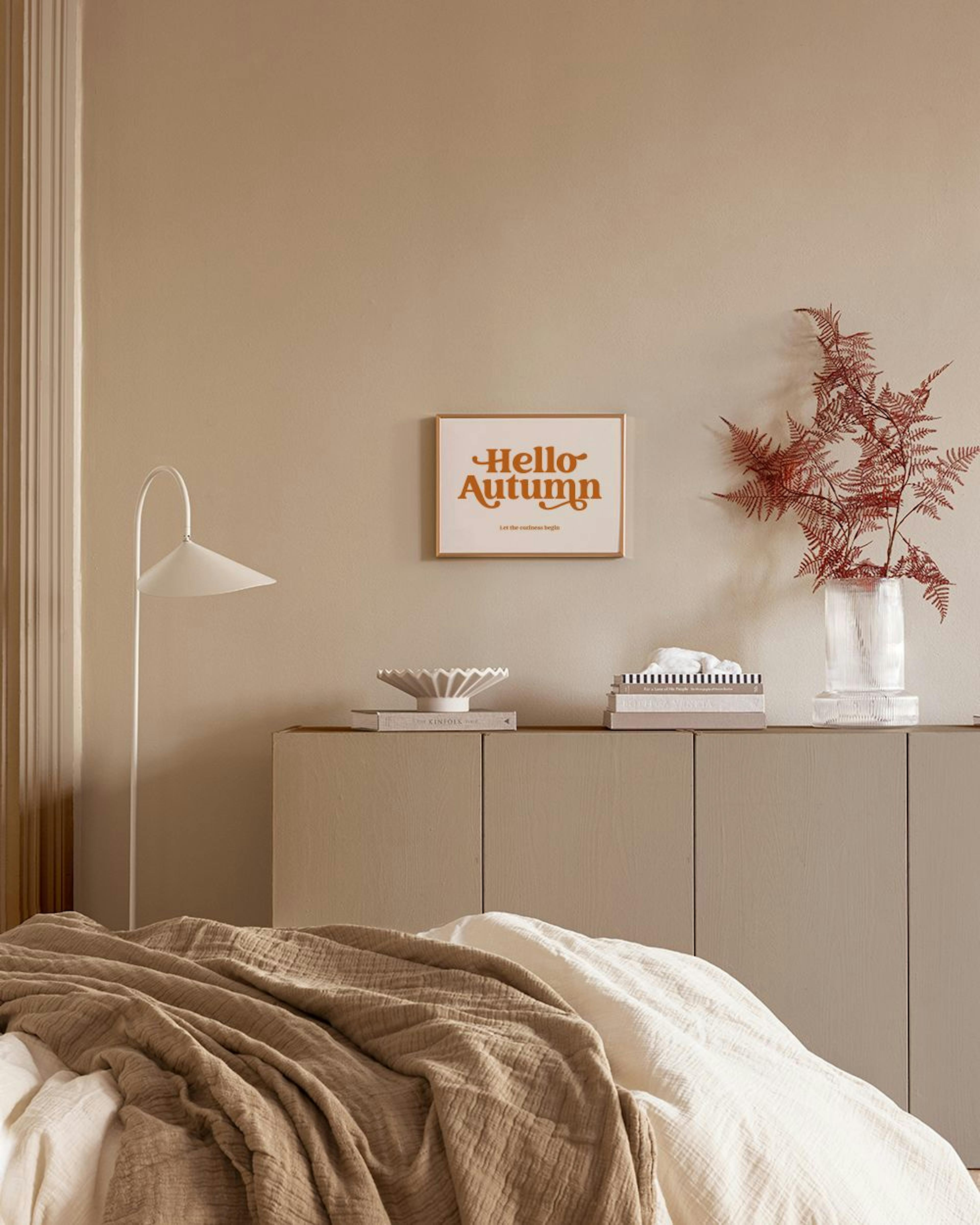 A poster with Hello Autumn in orange retro font on a white background, displayed above a cabinet in a neutral-toned bedroom.