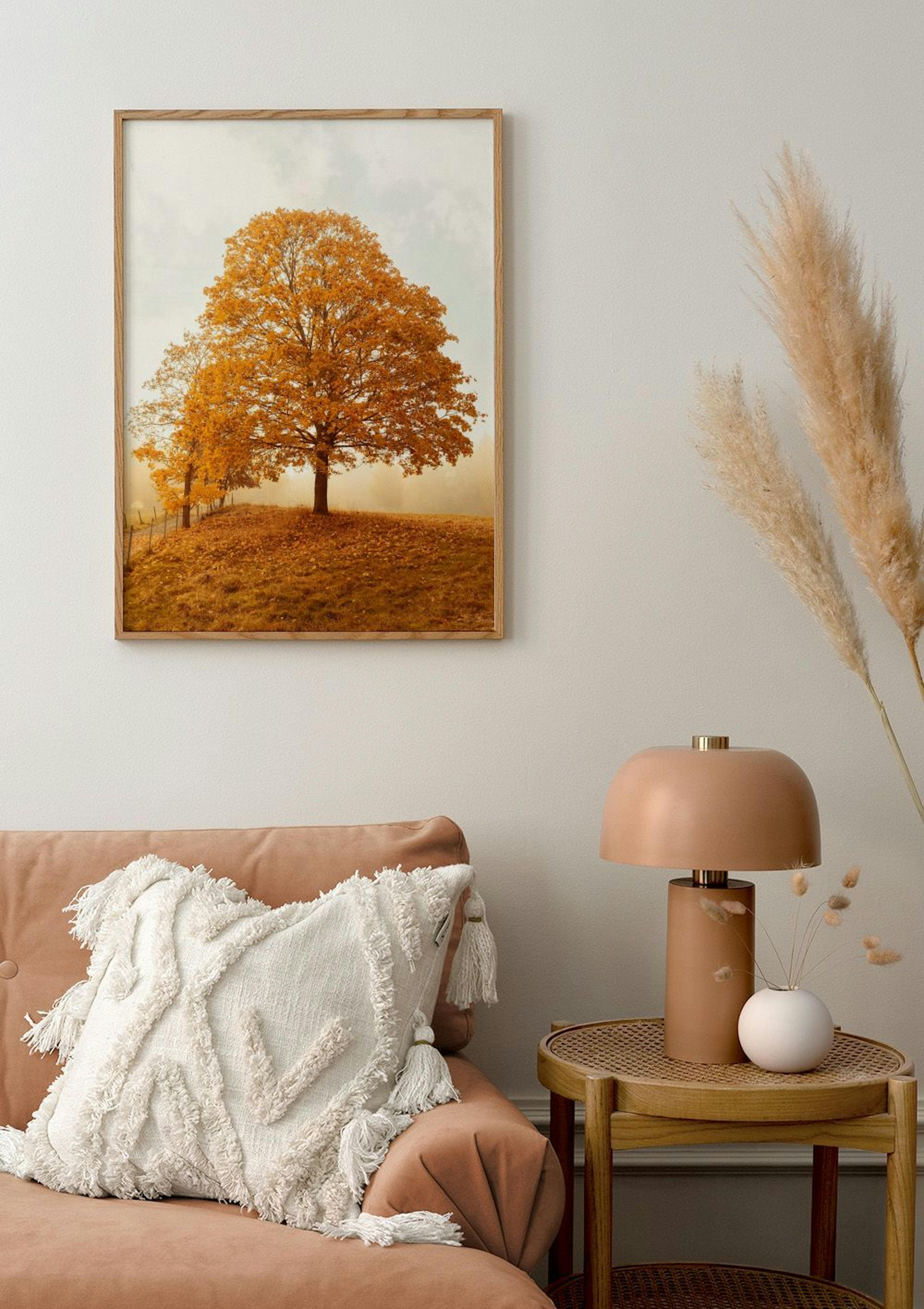 A poster of a vibrant orange autumn tree on a hill, hanging in a warm living room above a peach sofa.