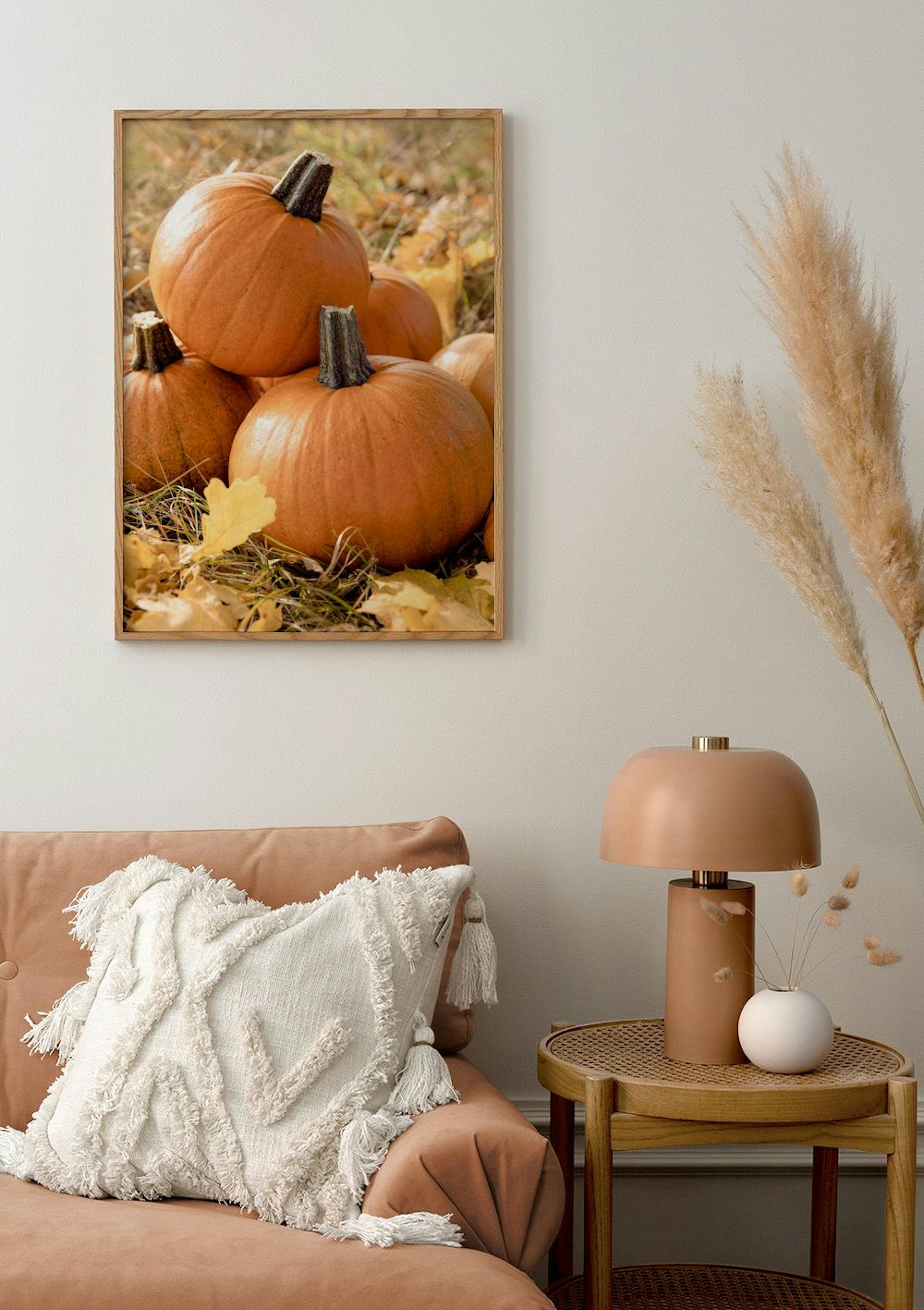 A poster featuring vibrant orange pumpkins nestled in autumn leaves and grass, displayed above a peach sofa.