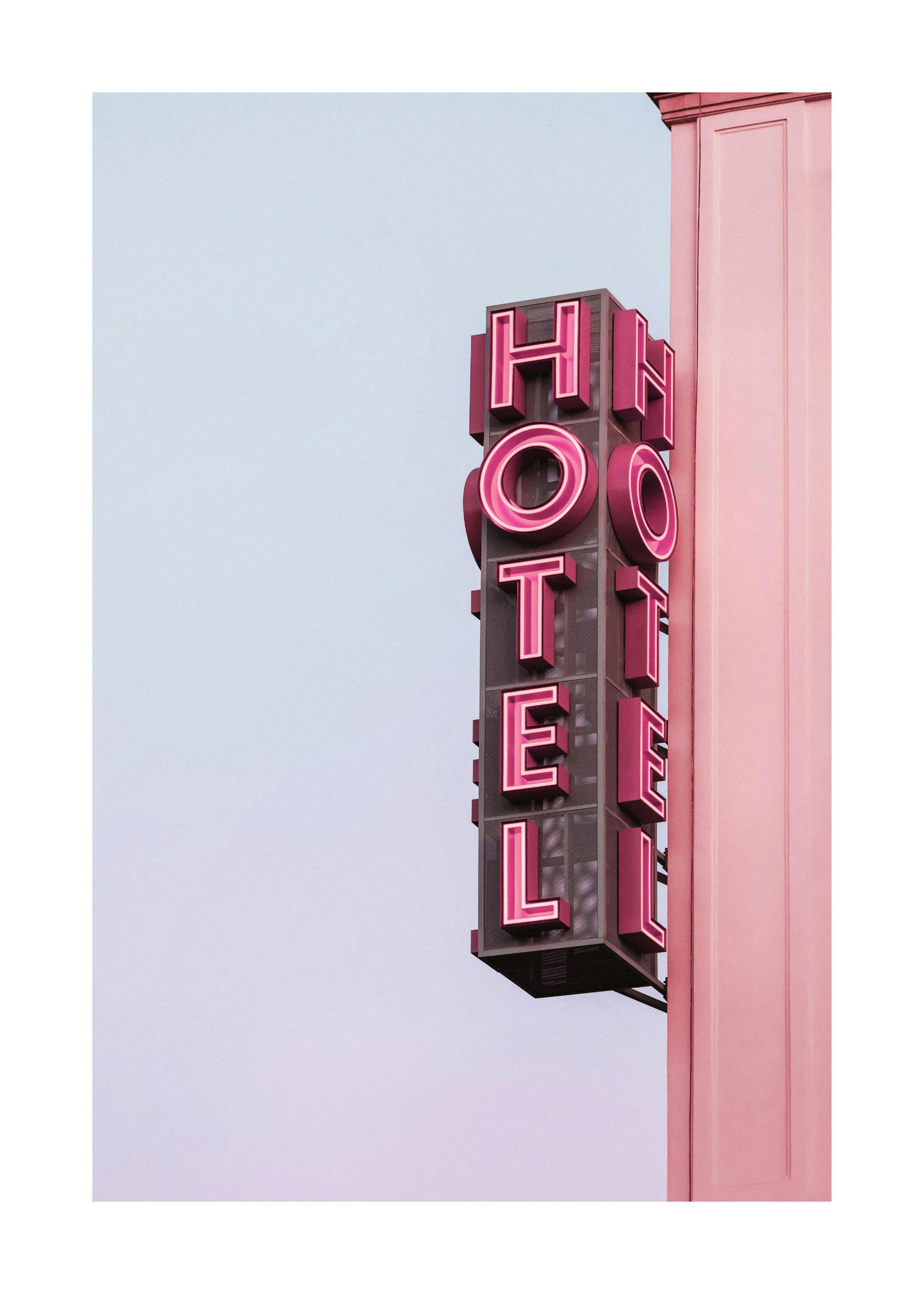 A poster featuring a pink neon HOTEL sign with a pink building column against a light blue sky.