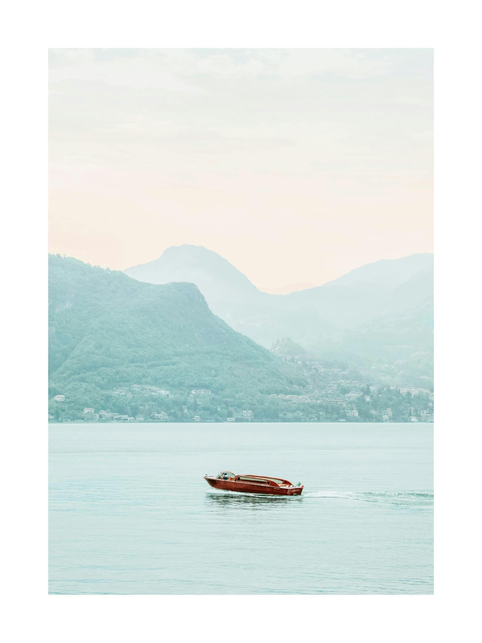 Un poster dun bateau rouge foncé sur leau turquoise avec des montagnes brumeuses en arrière-plan.
