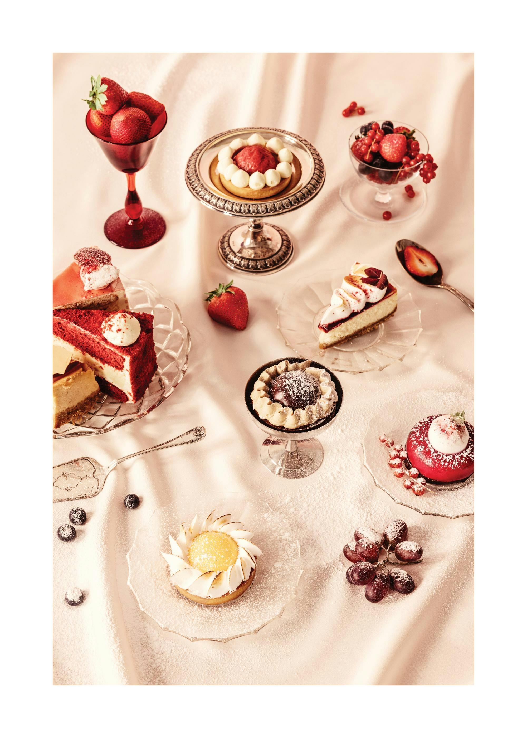 A poster displaying an assortment of red velvet cake, cheesecakes, and fruit tarts on a light pink cloth covered in powdered sug