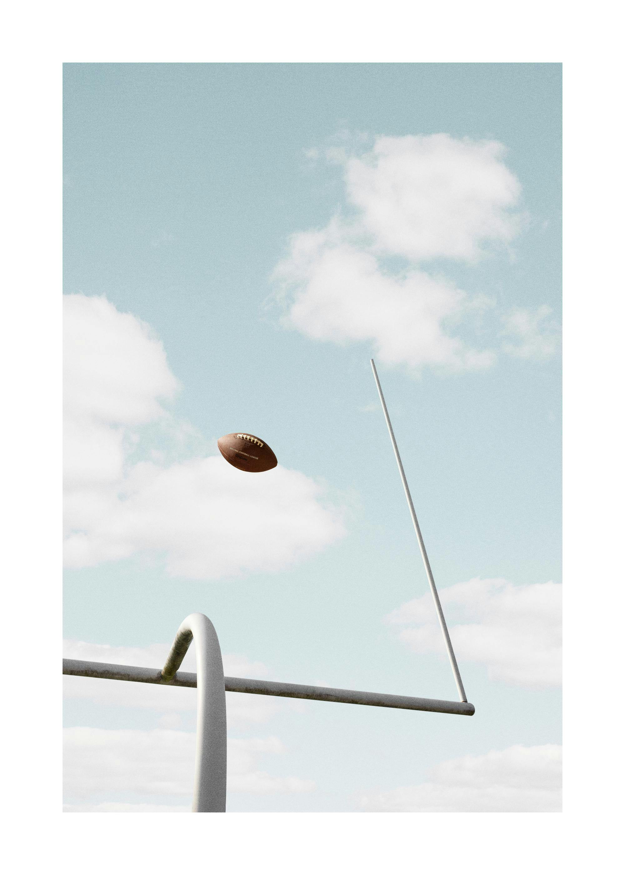 A poster of a football flying through goalposts against a cloudy blue sky, hanging in a minimalist room.