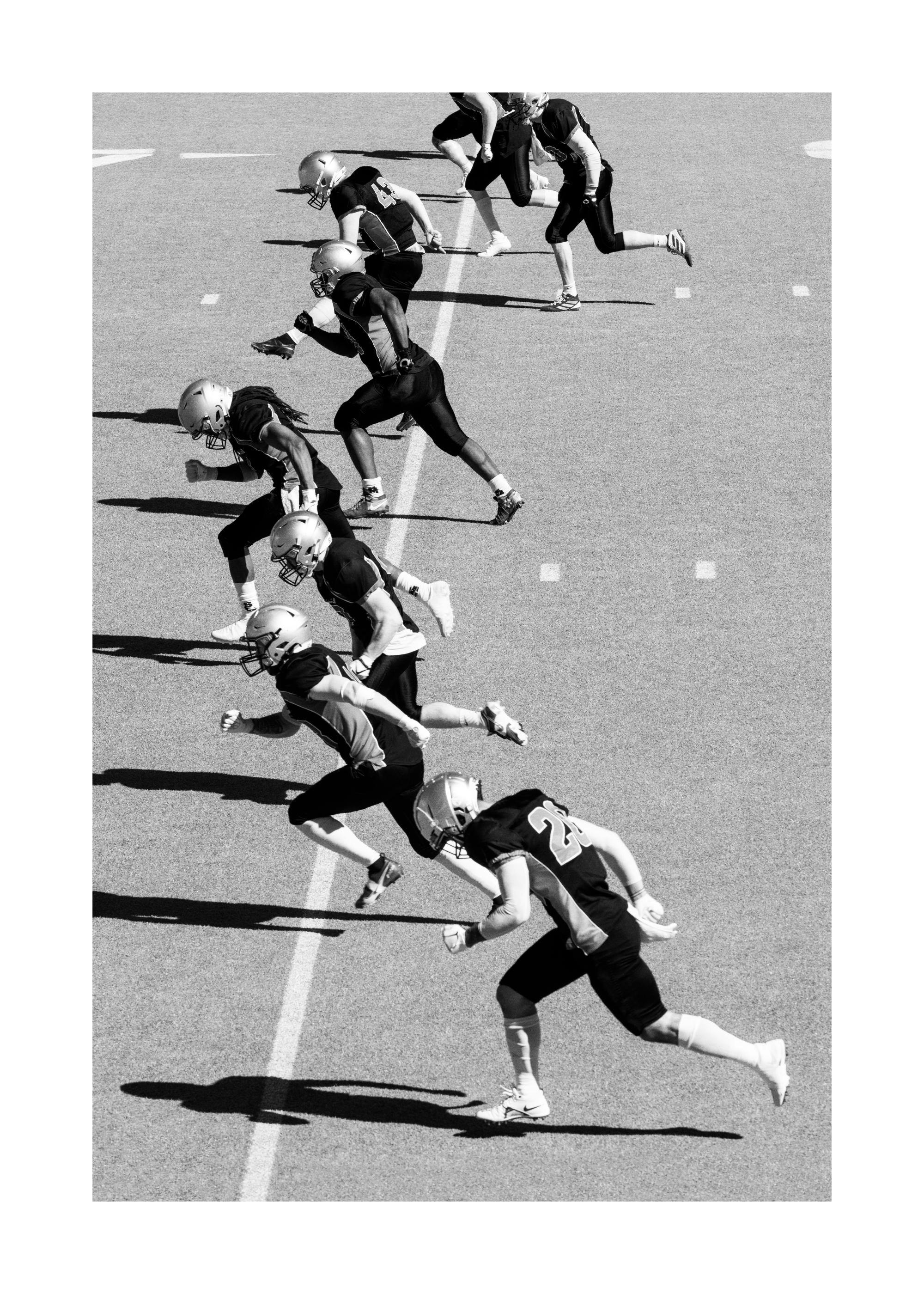 A poster of a black and white image of football players in full uniform running on a field.