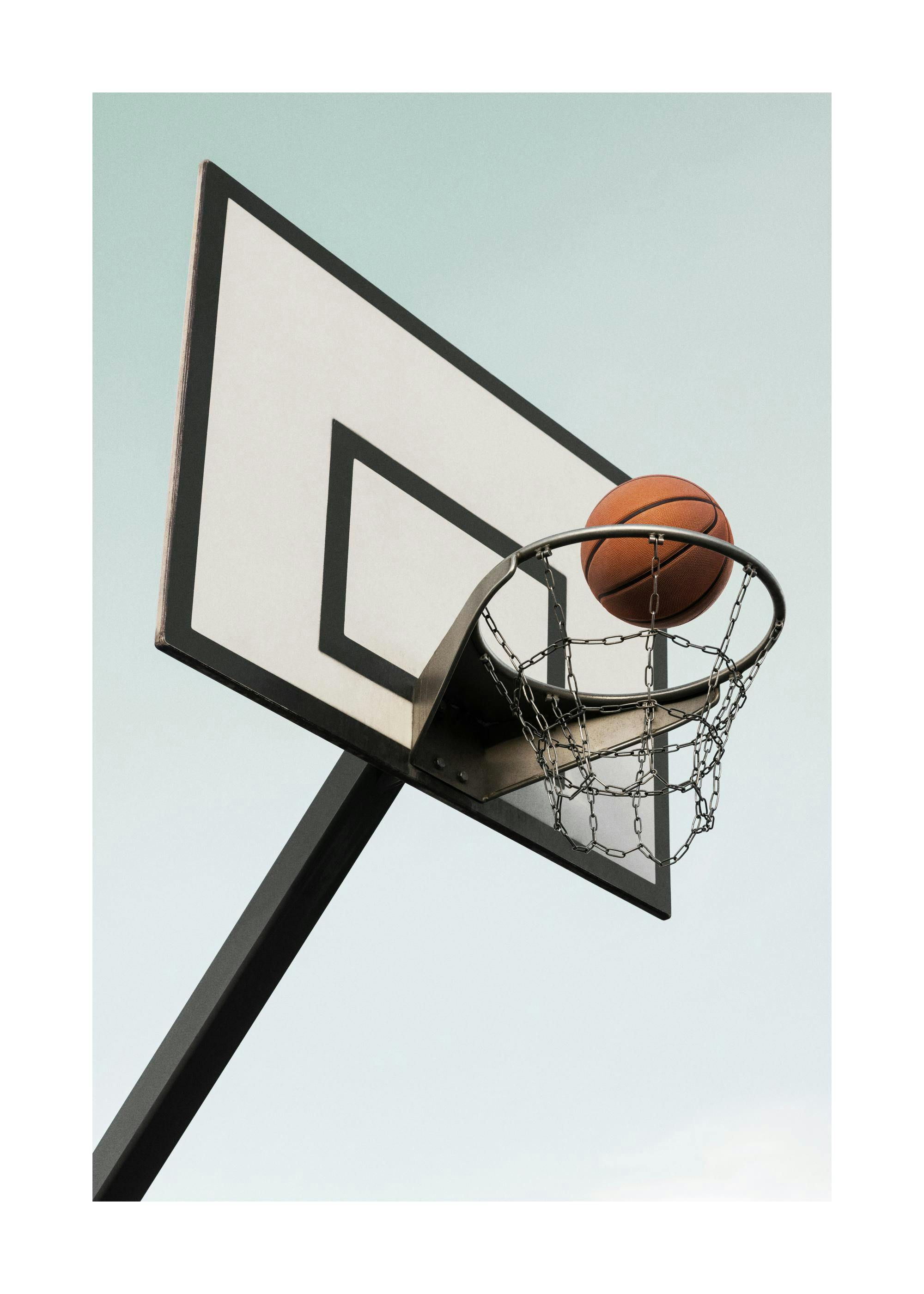 Un poster dun ballon de basketball sur le point de passer à travers un panier avec un filet métallique, sur fond de ciel clair.